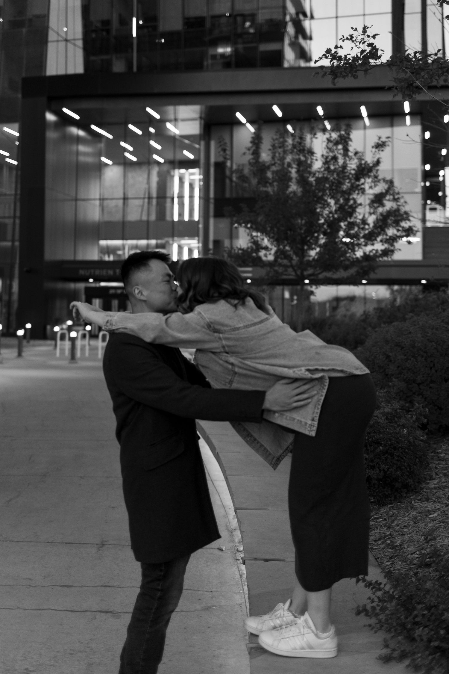 Black and white photo of a couple sharing a romantic dip kiss on a city sidewalk at night.