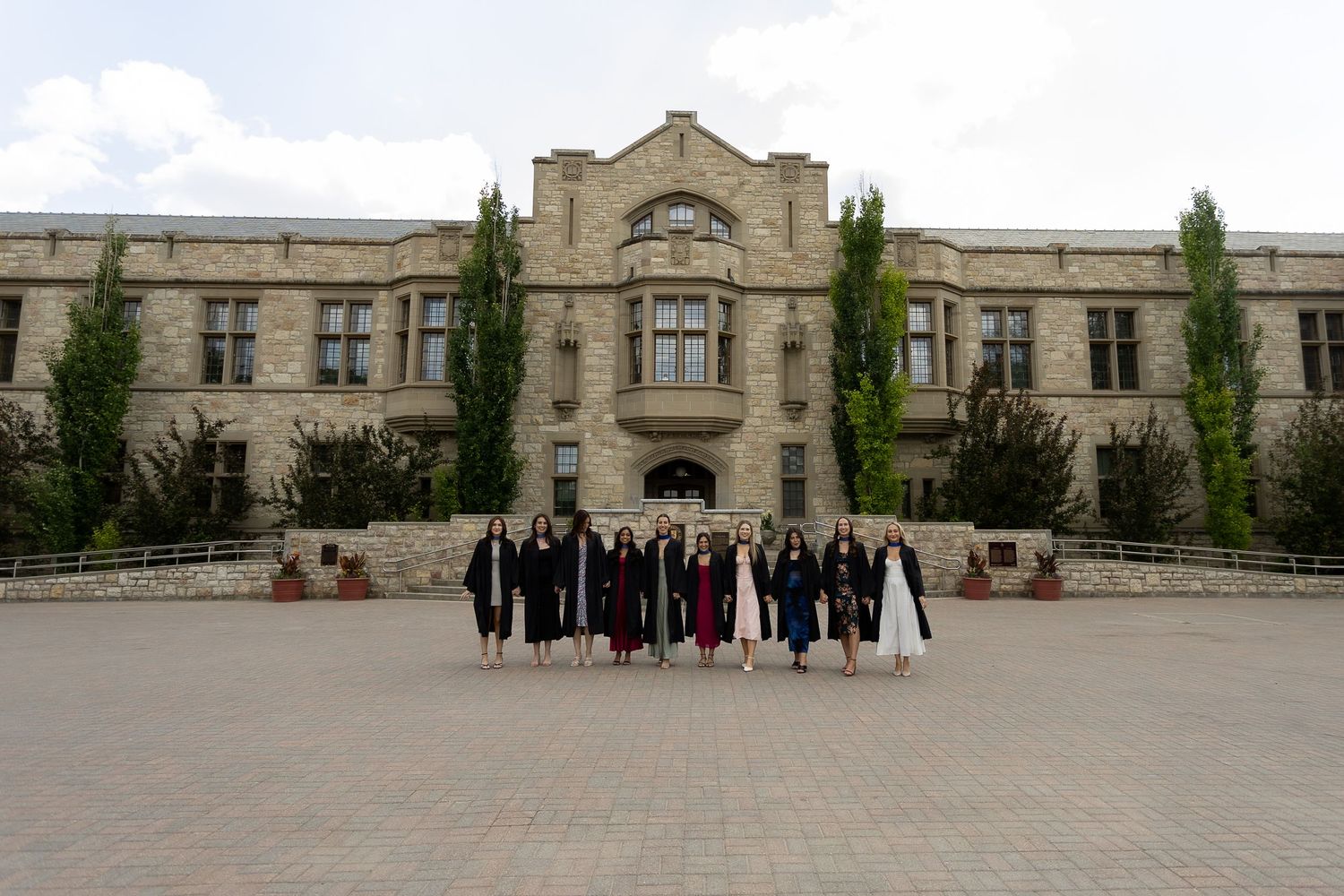 Group of graduates in caps and gowns posing in front of a historic stone university building.