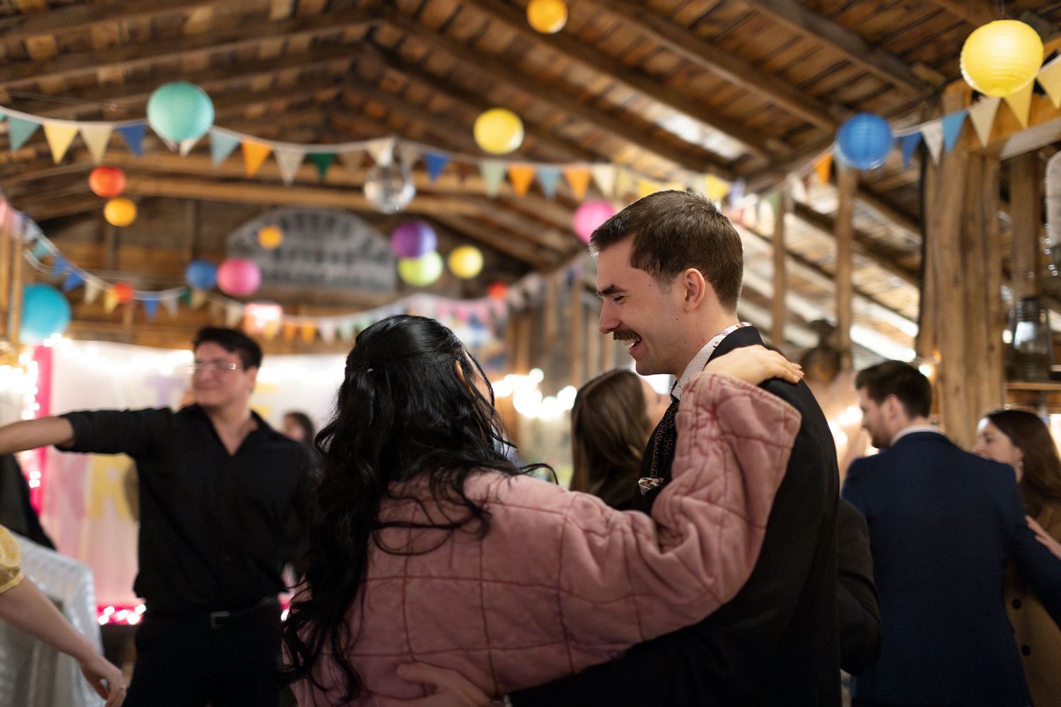 Couples dancing at a festive barn party decorated with colorful paper lanterns and bunting flags.