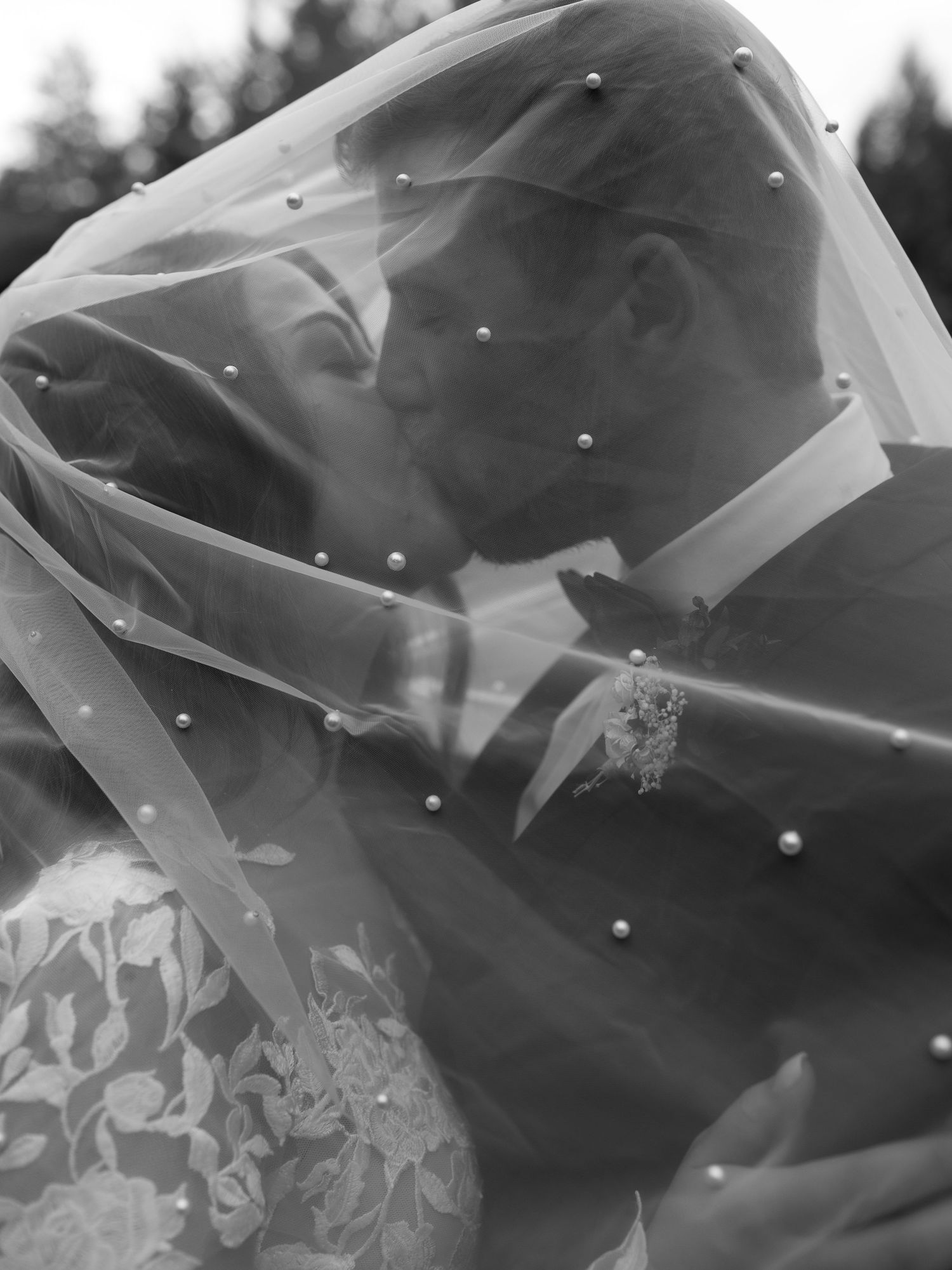 Black and white photo of romantic kiss under a crystal-studded veil.