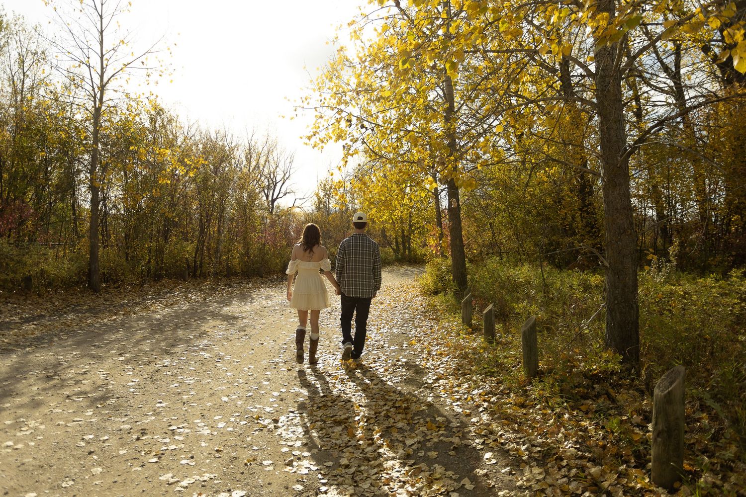 Couple walks down sunlit path through autumn trees.