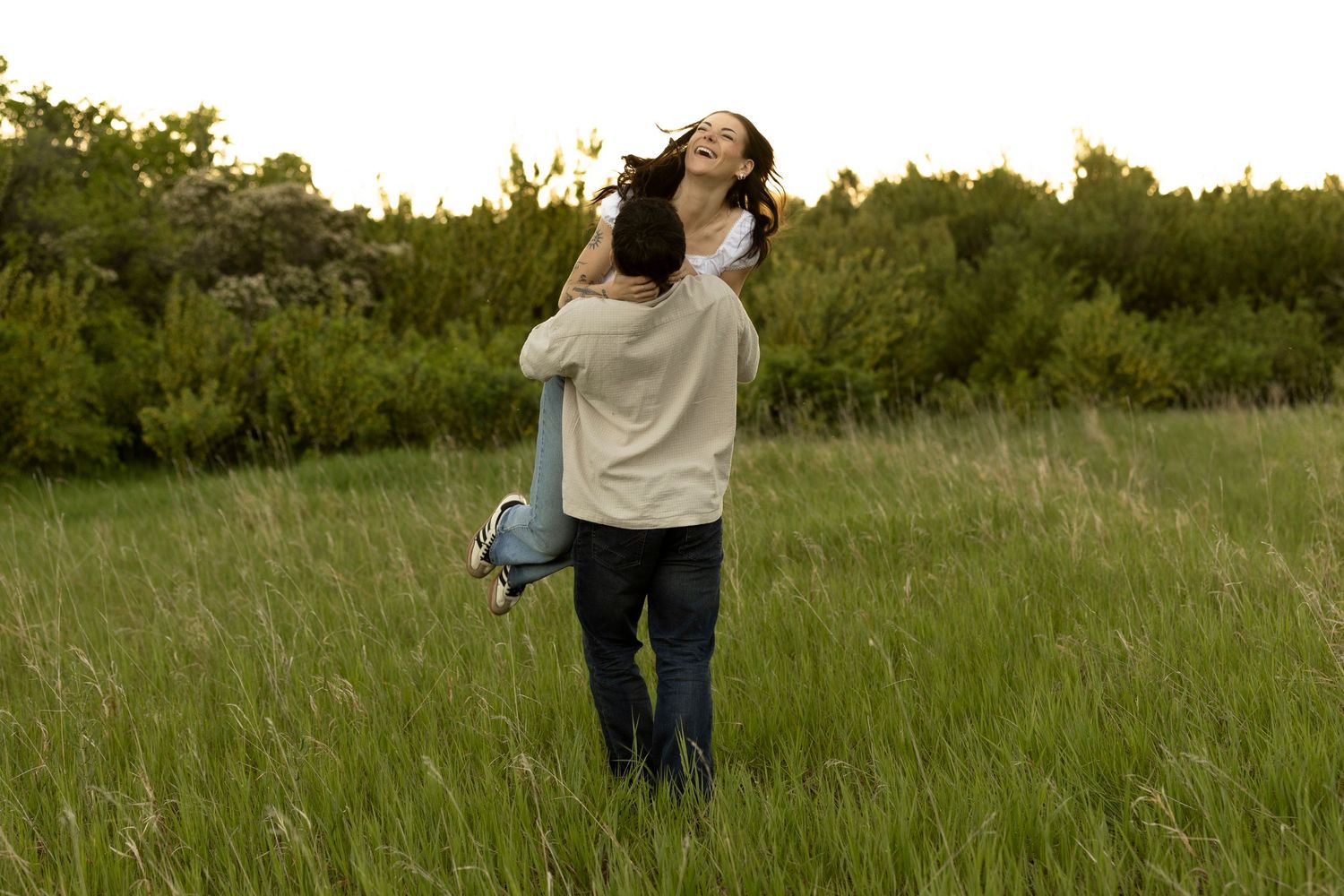 Couple embracing in a lush green field, man lifting woman as she laughs with joy outdoors.