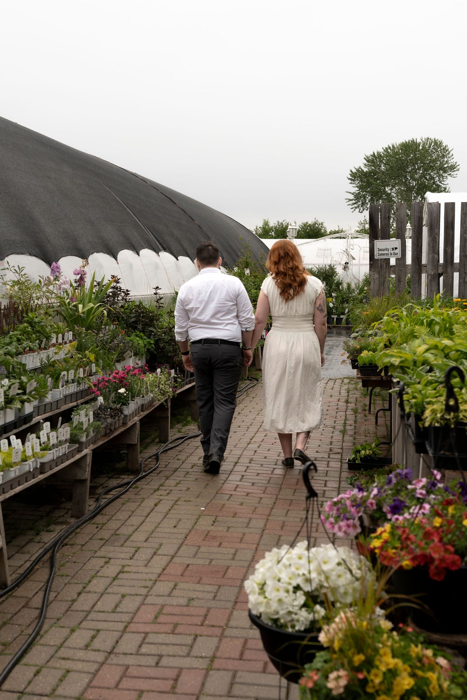 Couple walking hand in hand through a lush garden nursery with colorful flowers and plants on a cloudy day.