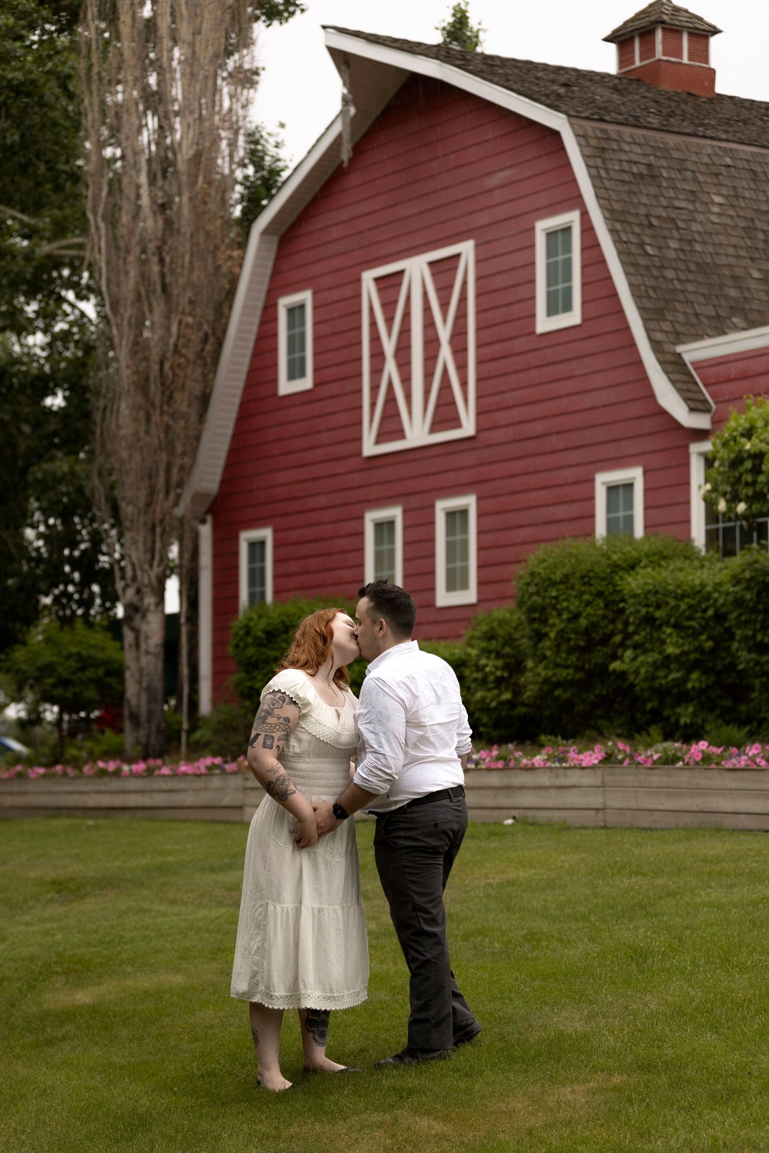 Couple embracing on green lawn with a classic red barn backdrop during their wedding day.