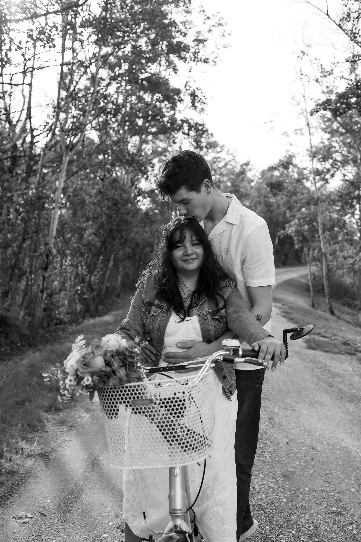 A couple shares an intimate moment on a dirt path with a decorated bicycle basket.