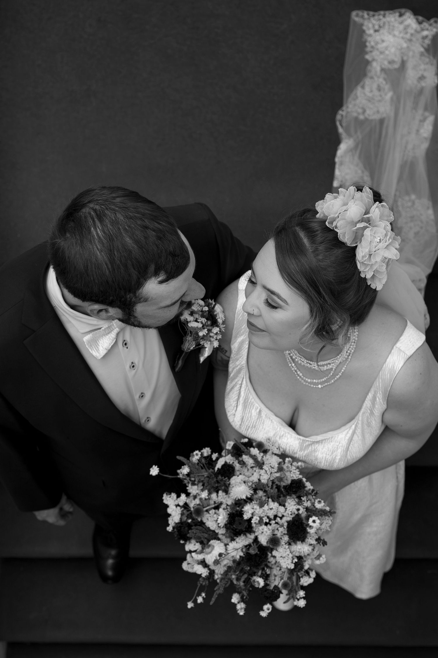 Aerial black and white photo of bride and groom sharing a kiss, bride holding a floral bouquet on their wedding day.