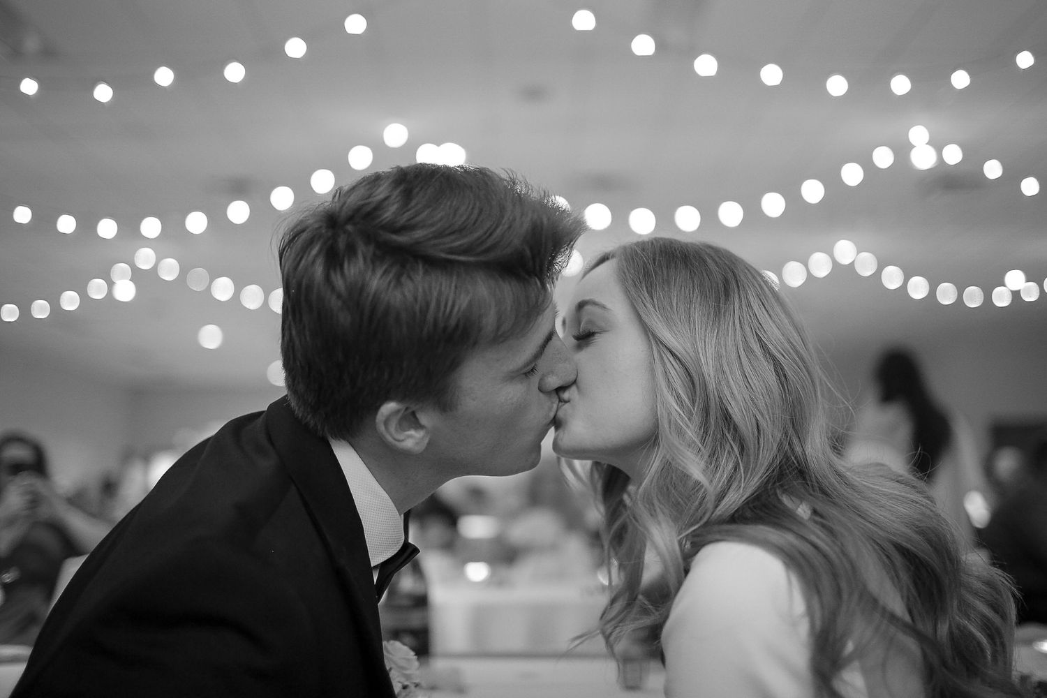 A black and white photo montage showing couples kissing under romantic string lights at a wedding reception.