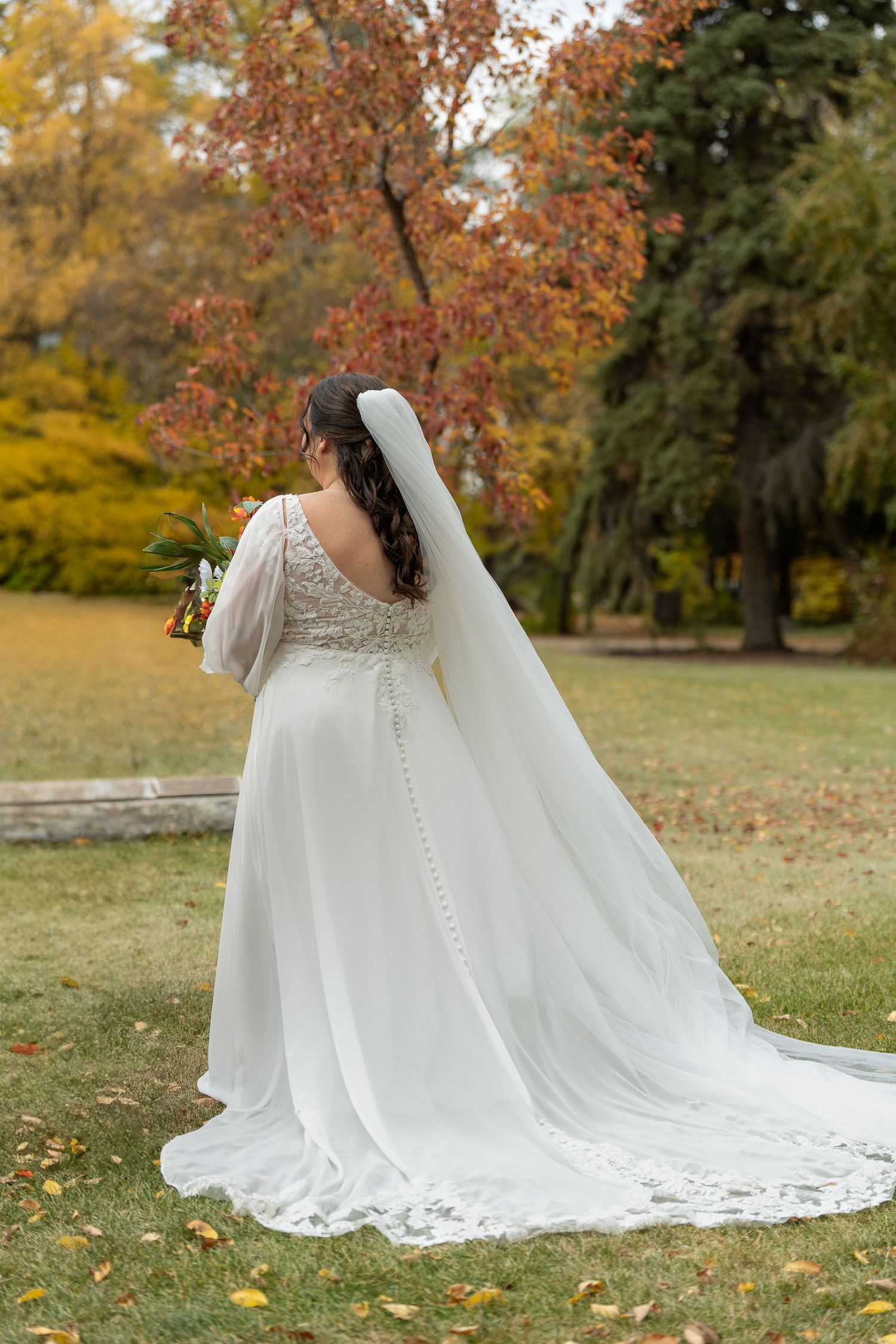 Wedding dress train with intricate lace details spread across autumn grass.
