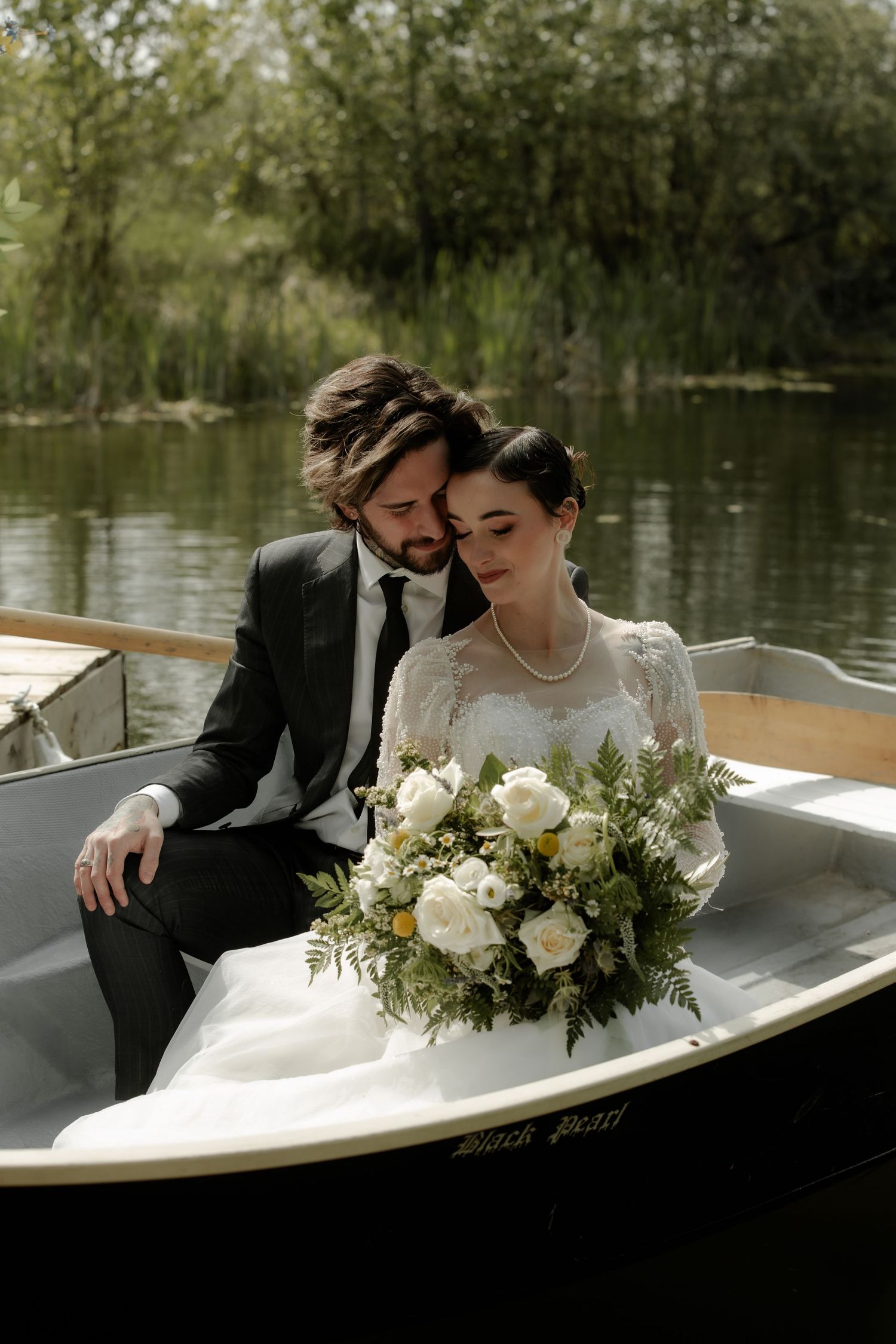 Romantic couple moment in a wooden rowboat on a serene lake with wedding flowers.