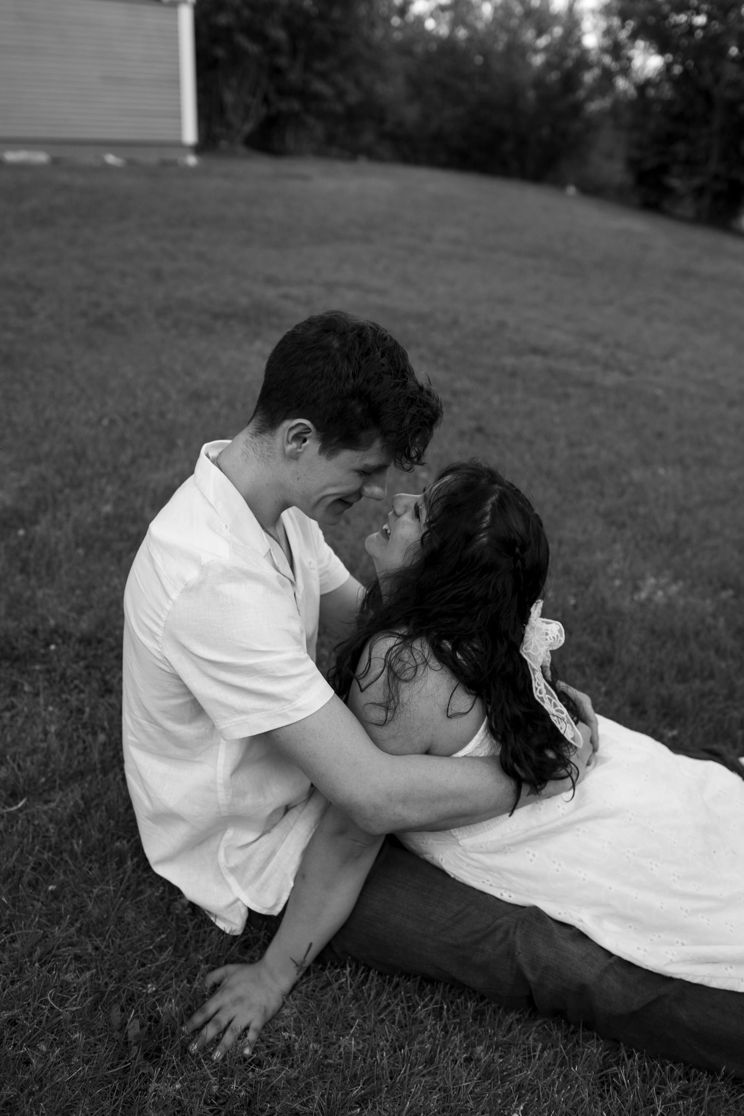A romantic couple lying in grass sharing an intimate moment outdoors.