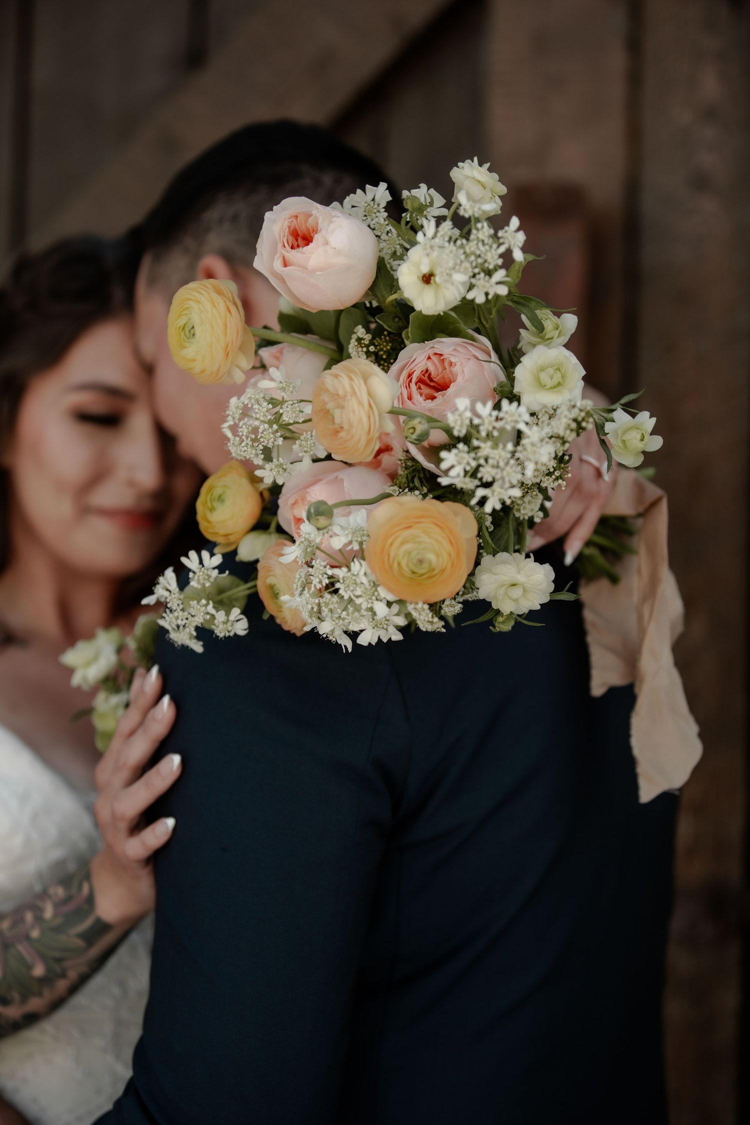 Delicate peach and white flowers accent a wedding couple's romantic portrait at wedding at Cork & Crate Estates in Olds, Alberta.