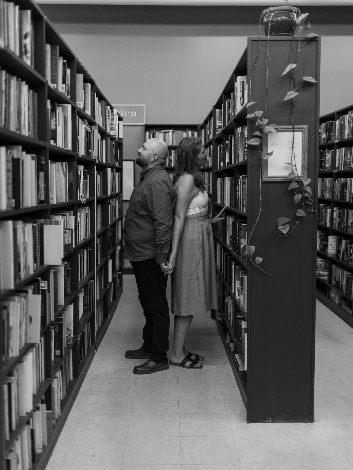 Black and white photo of figures standing between tall library bookshelves.
