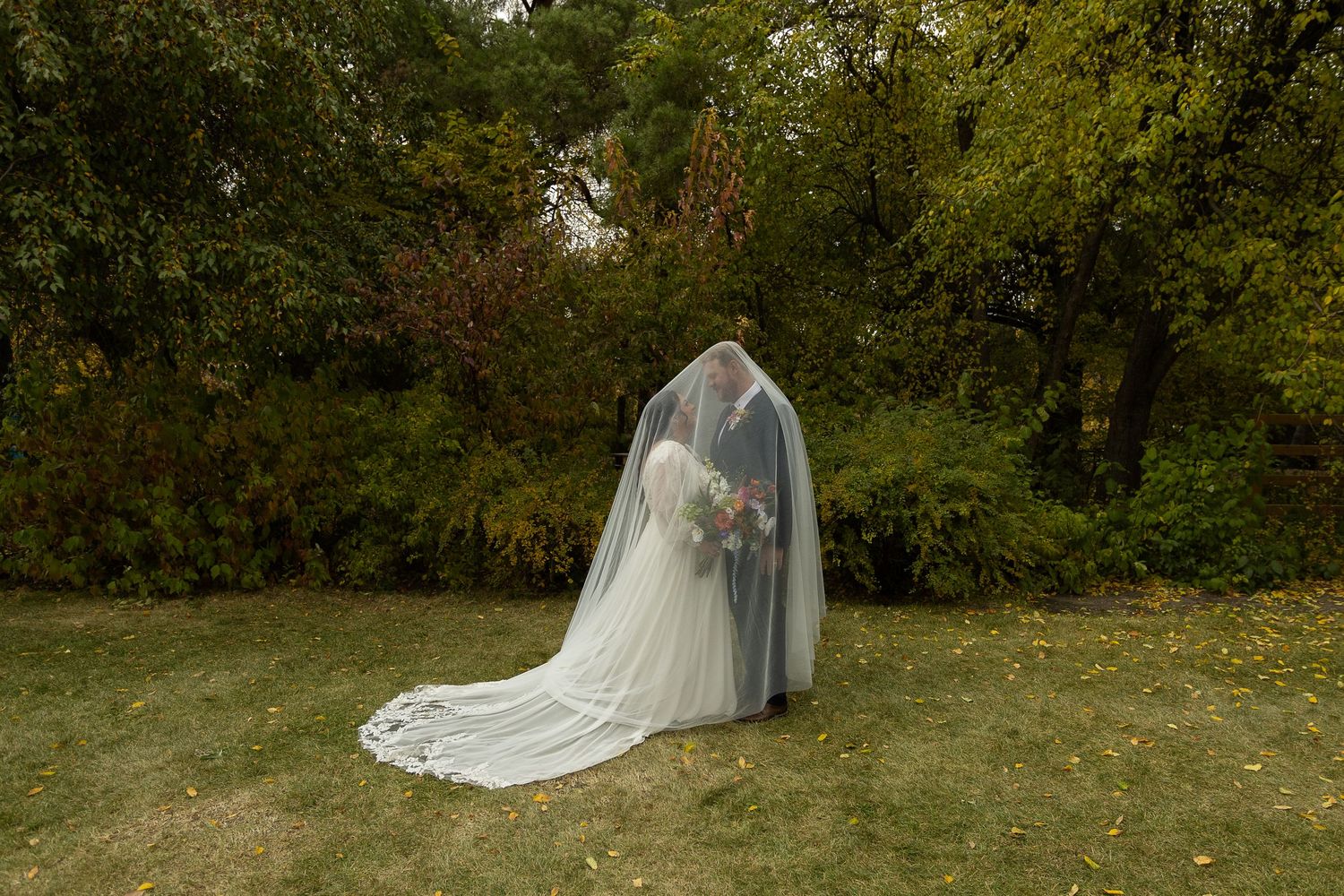 A couple in wedding attire poses together in a scenic outdoor garden setting during their special day at the Forestry Farm Zoo.