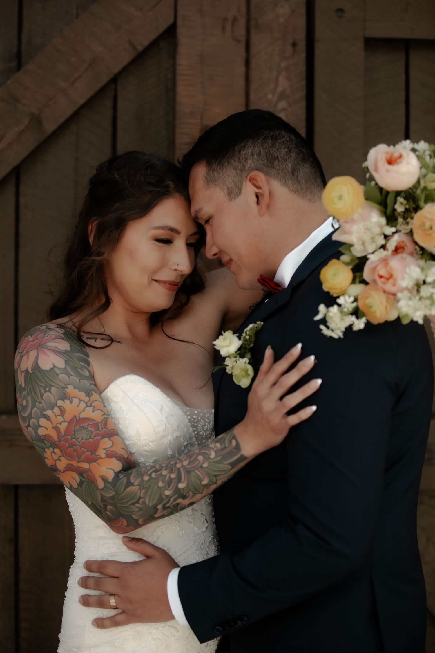 A couple embraces during their wedding with peach and white floral decorations in the background.
