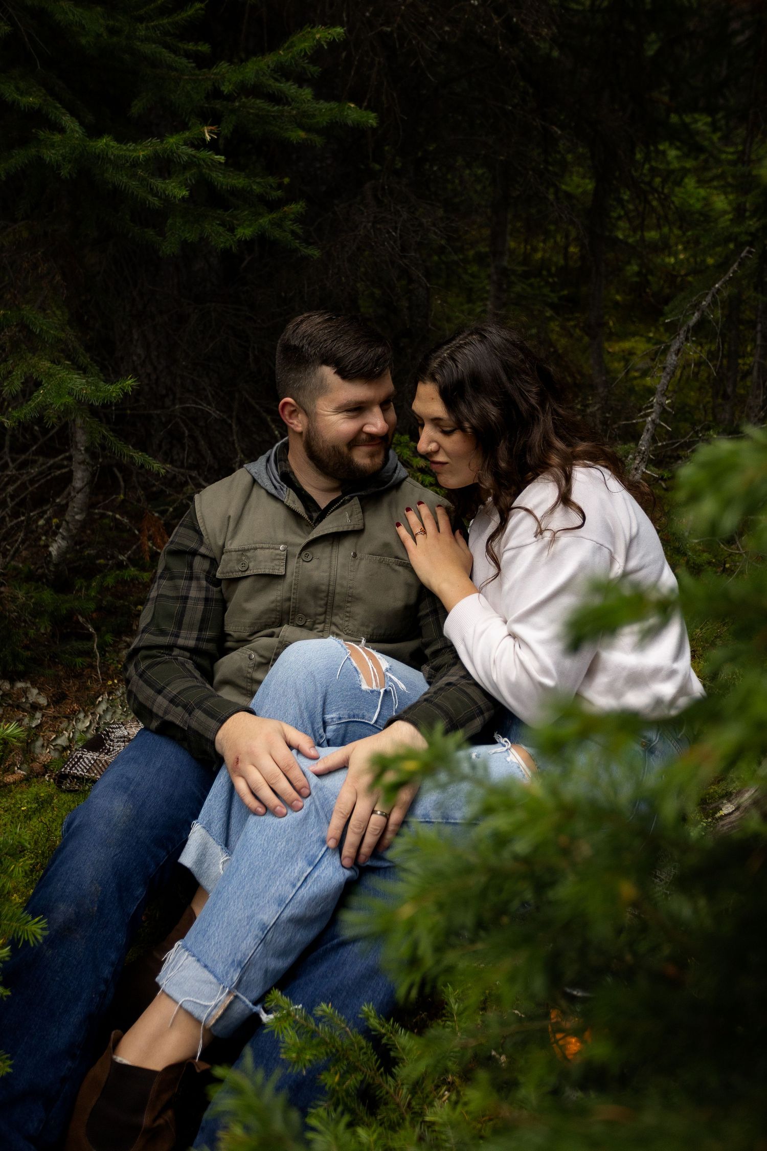 Romantic couple sitting together among evergreen trees in a dark forest setting.