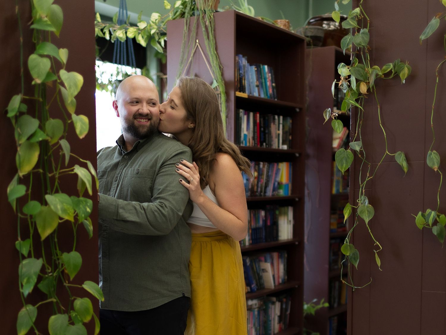 A couple embraces in a library between rows of bookshelves.