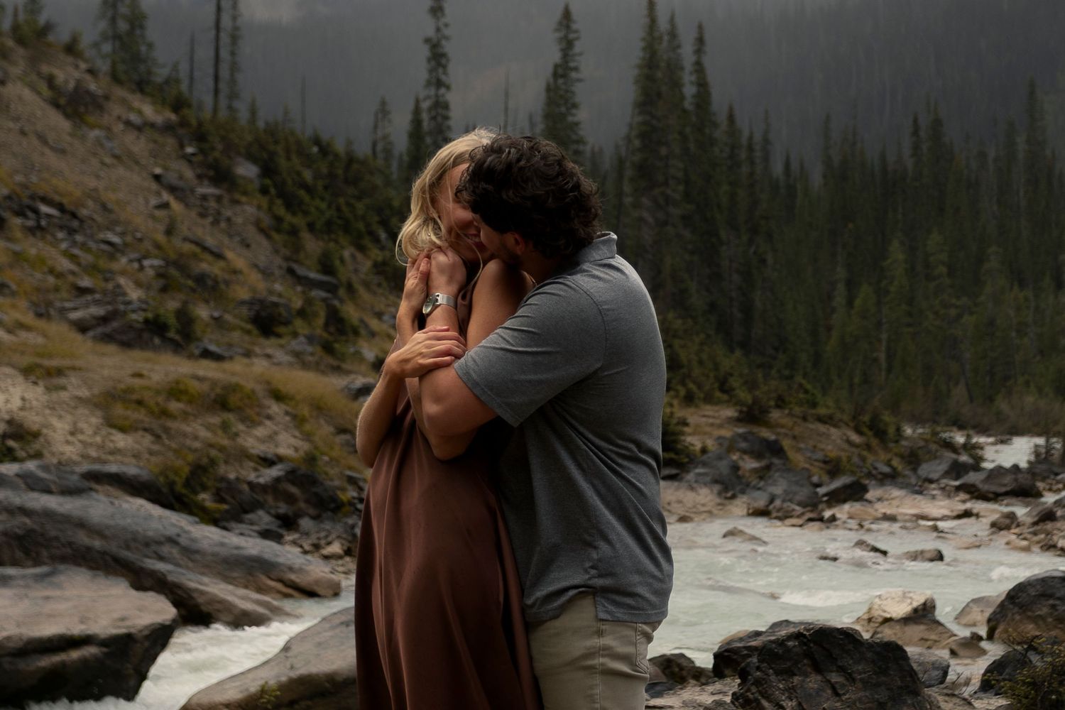 A couple embraces against a scenic mountain backdrop during golden hour at Takakkaw Falls.