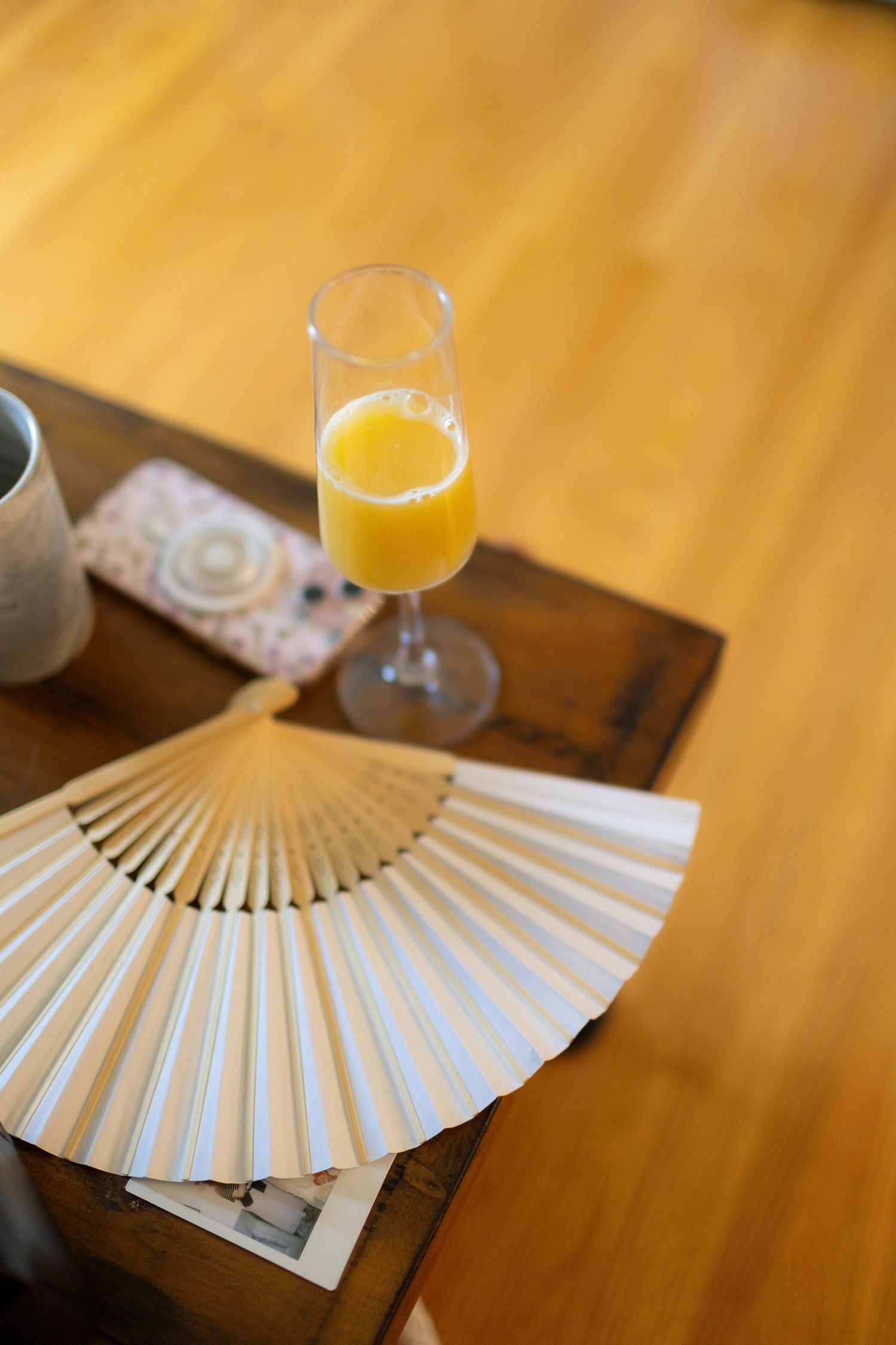 White paper fans and mimosas arranged on wooden table at wedding reception.