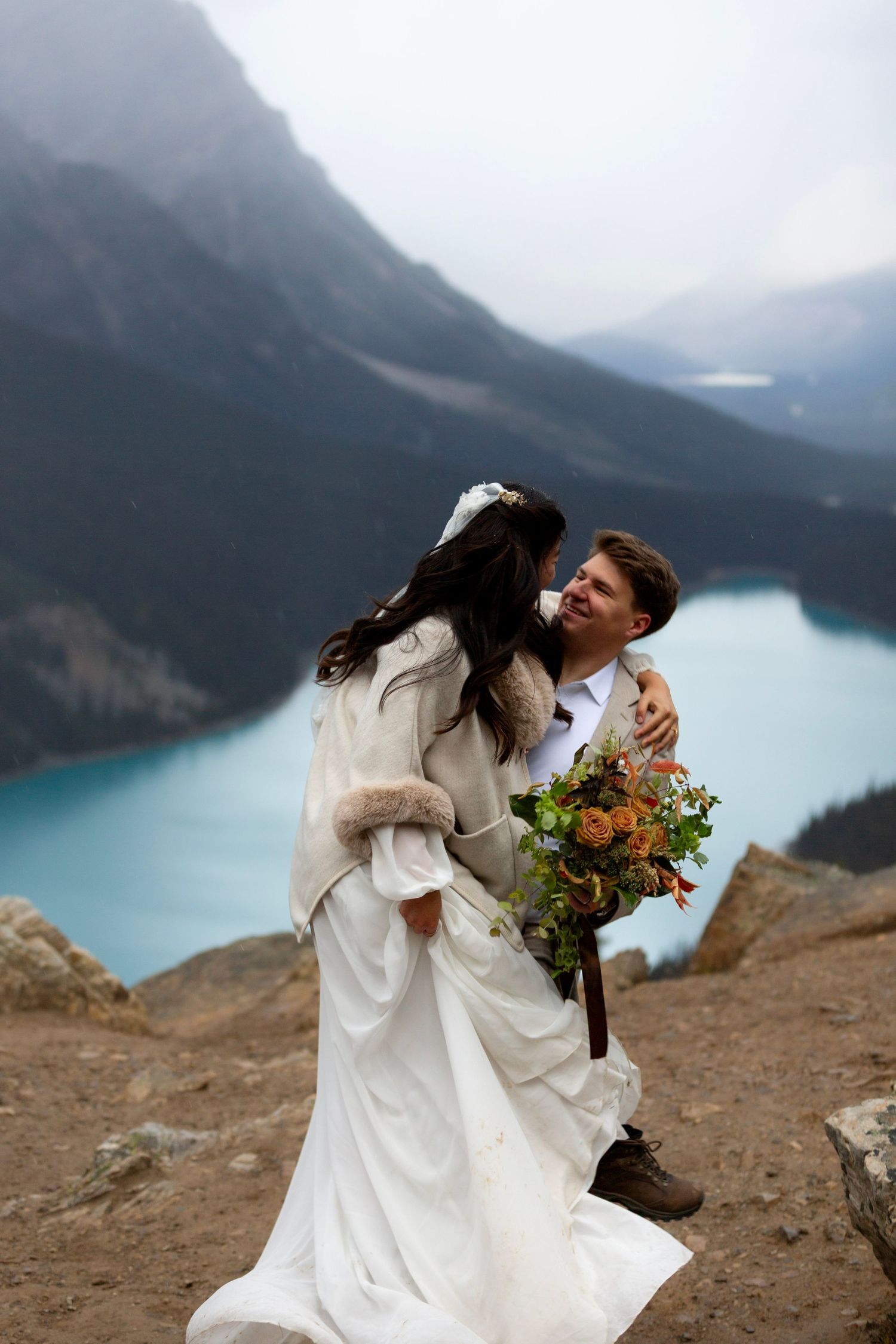 A romantic wedding photoshoot against a stunning turquoise mountain lake with dramatic cloudy skies in the background at Peyto Lake in Banff