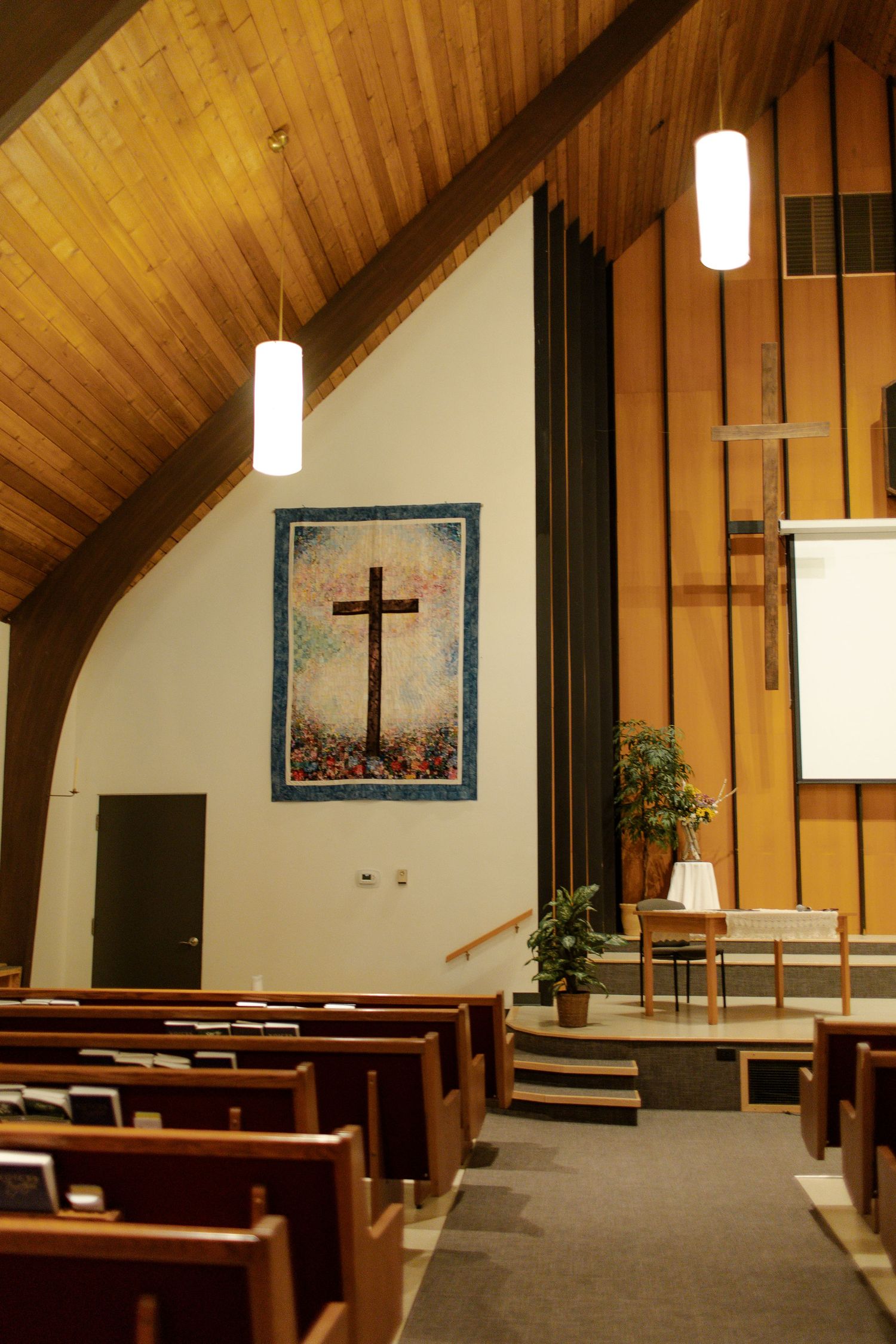 Interior of a church sanctuary with wooden ceiling, pews and cross on wall.