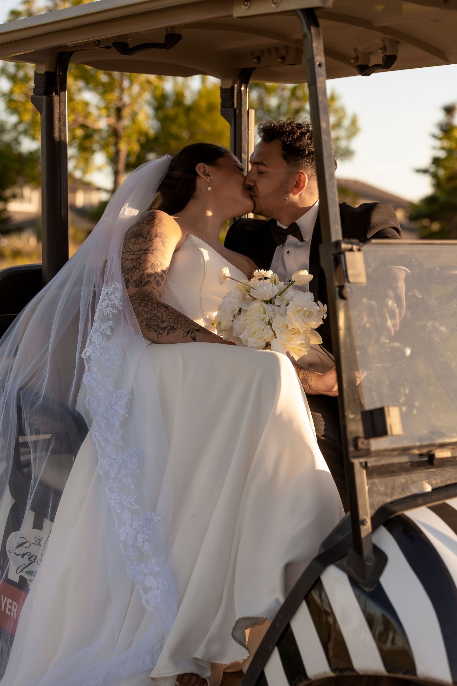 Newlyweds share a romantic moment in a golf cart at sunset.