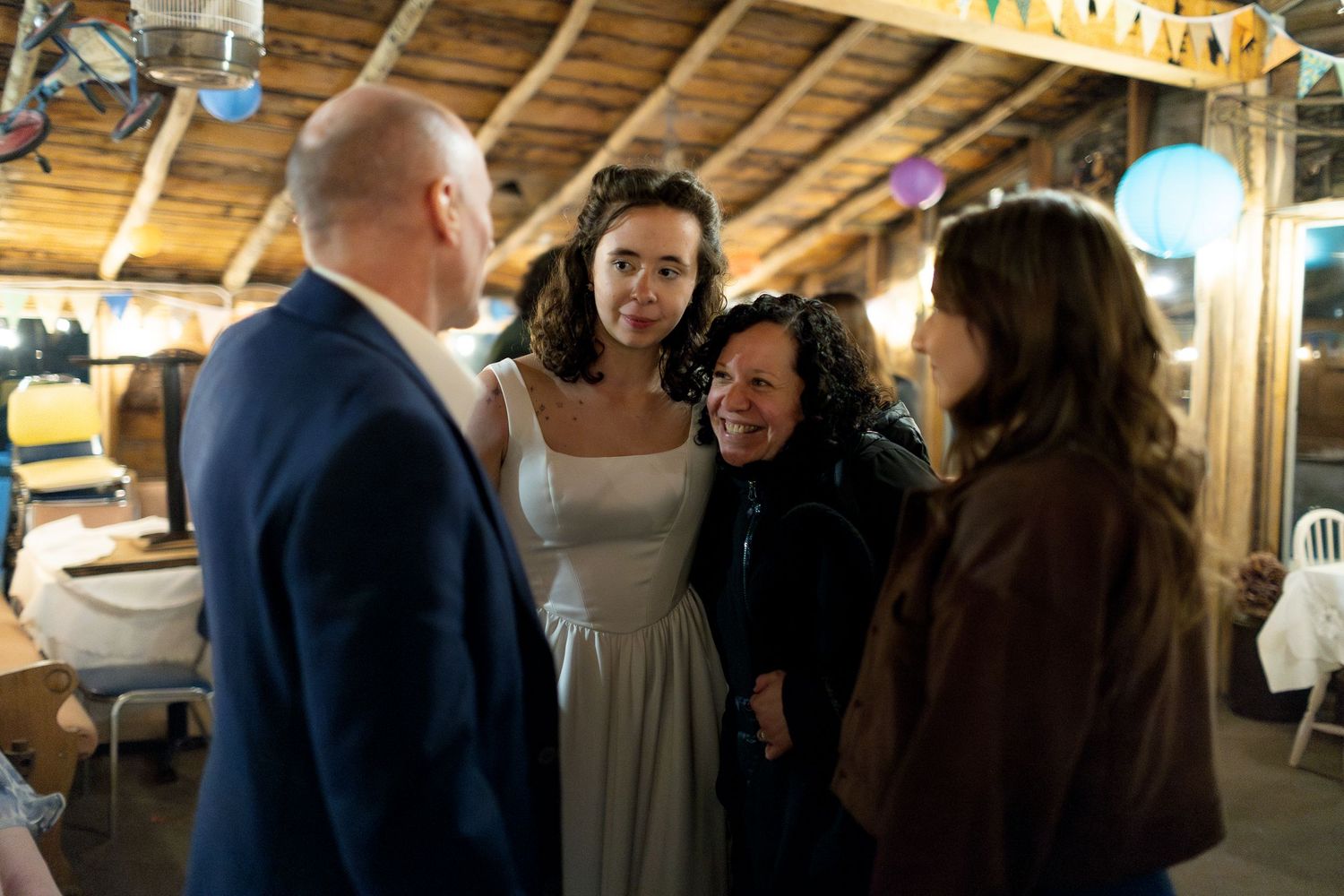 Group of people in formal attire conversing at a rustic indoor wedding reception venue.