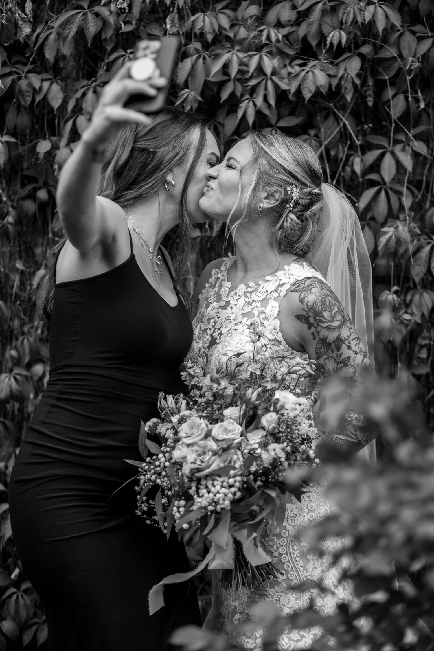 Two people take a selfie together while holding a bouquet of flowers.
