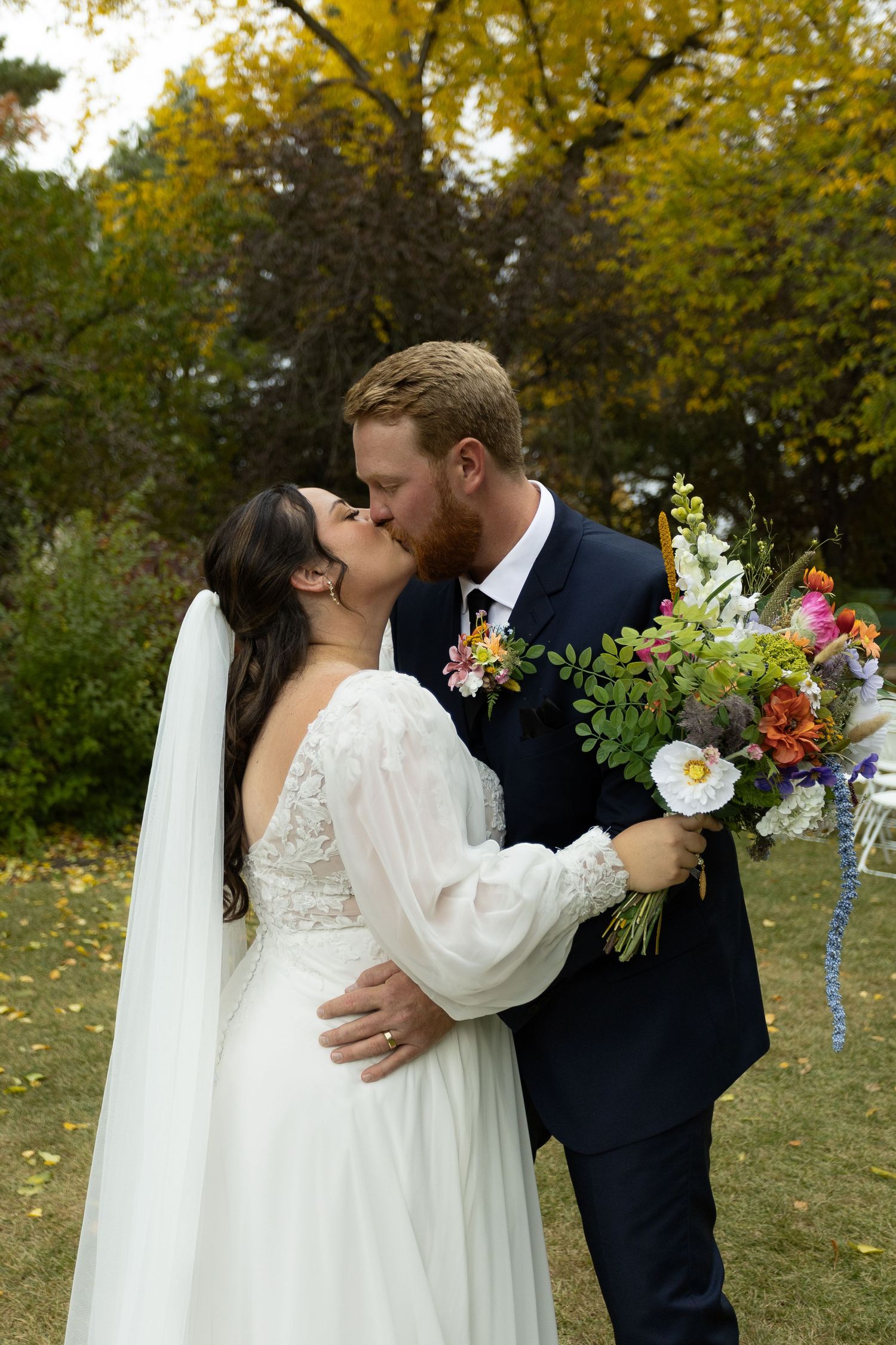 Autumn wedding portrait with colorful bouquet and fall foliage in background.