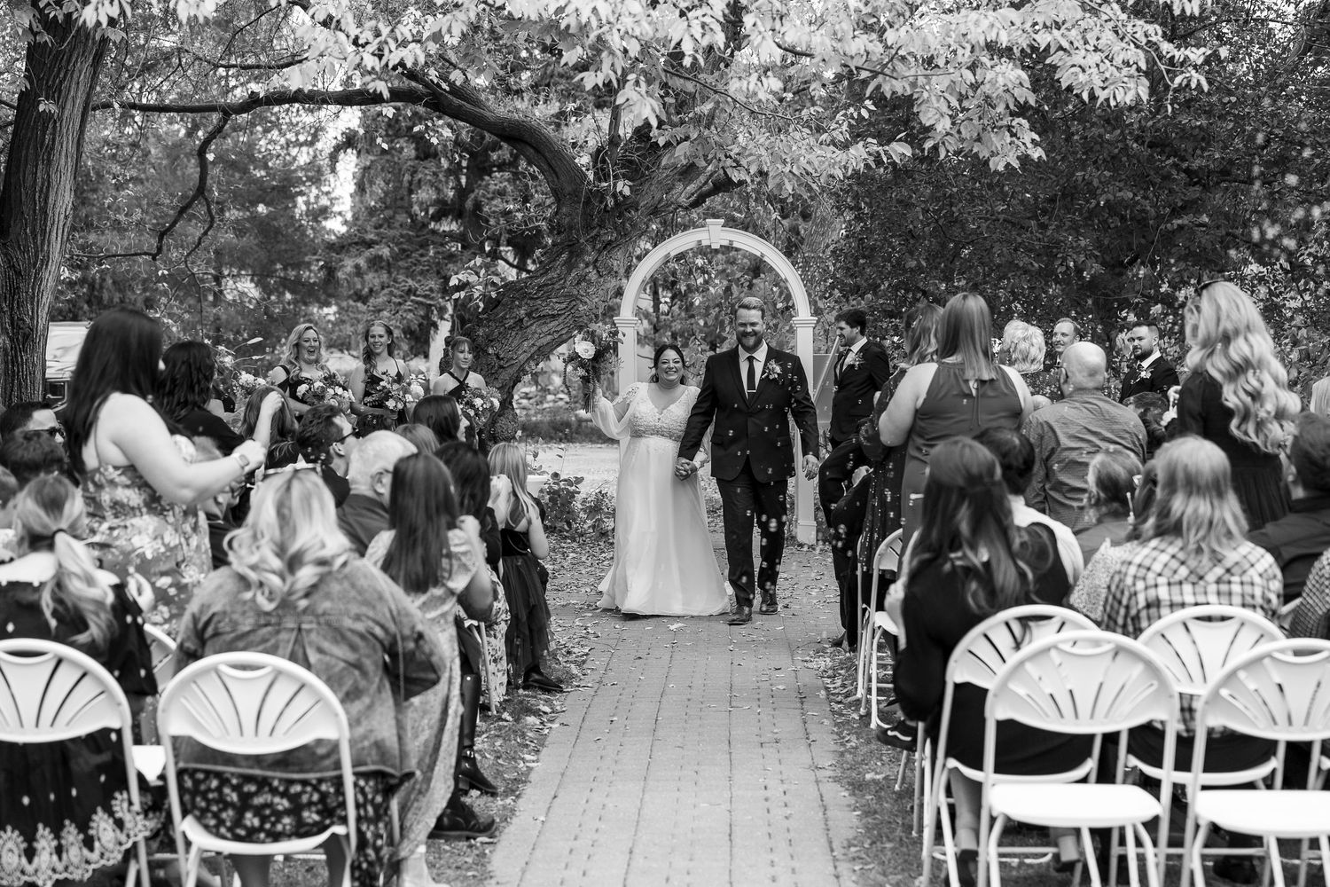 Outdoor wedding ceremony setup with white chairs under trees at the Forestry Farm in Saskatoon, Saskatchewan.