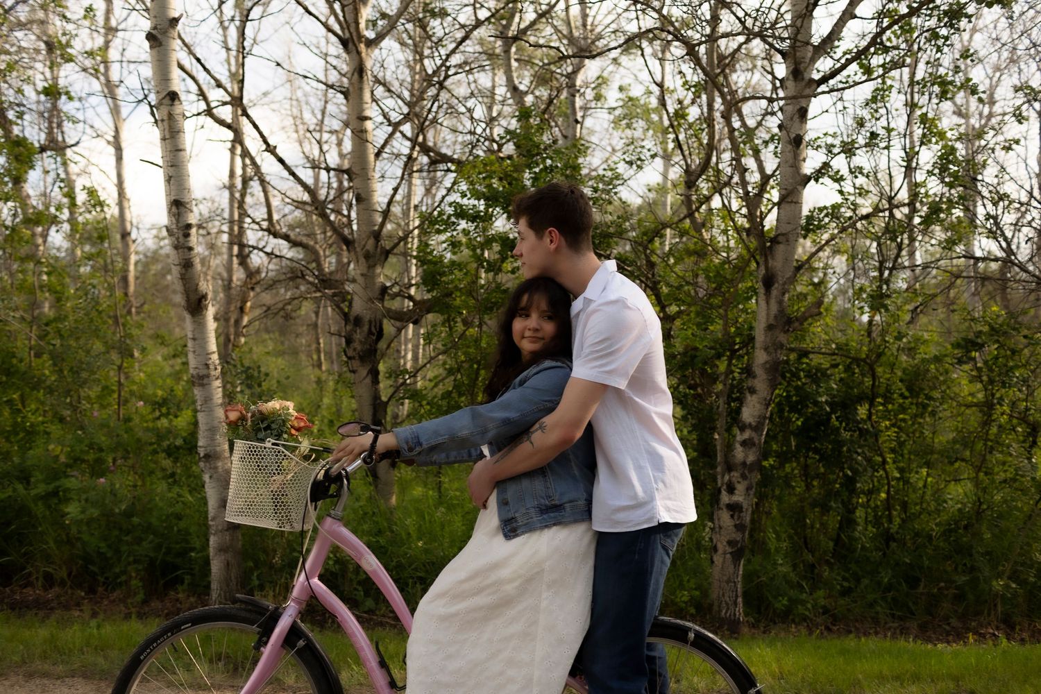Couple embracing near a pink bicycle with flower basket in a lush green park setting.