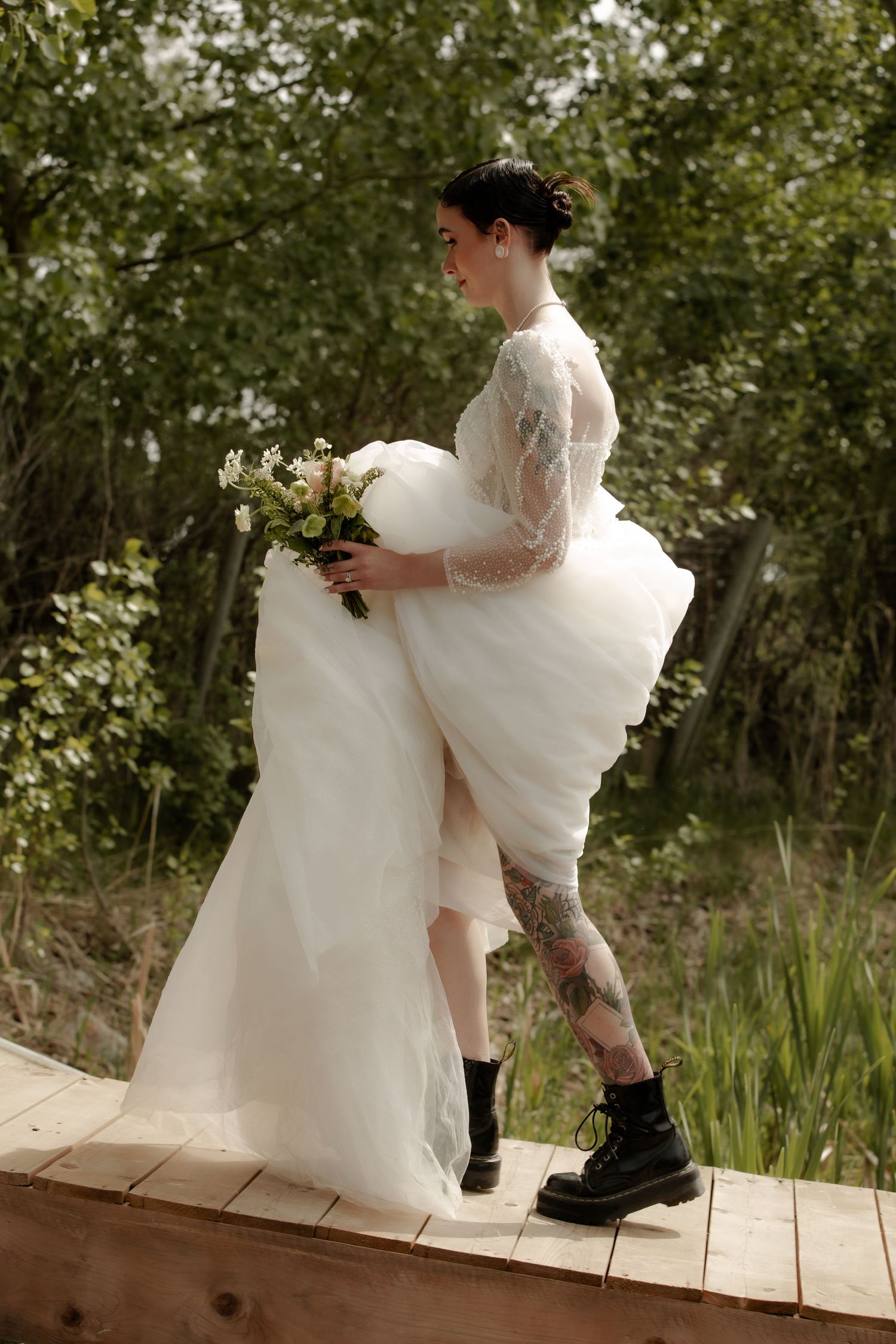 Couple in wedding attire sitting together on wooden dock by the water.