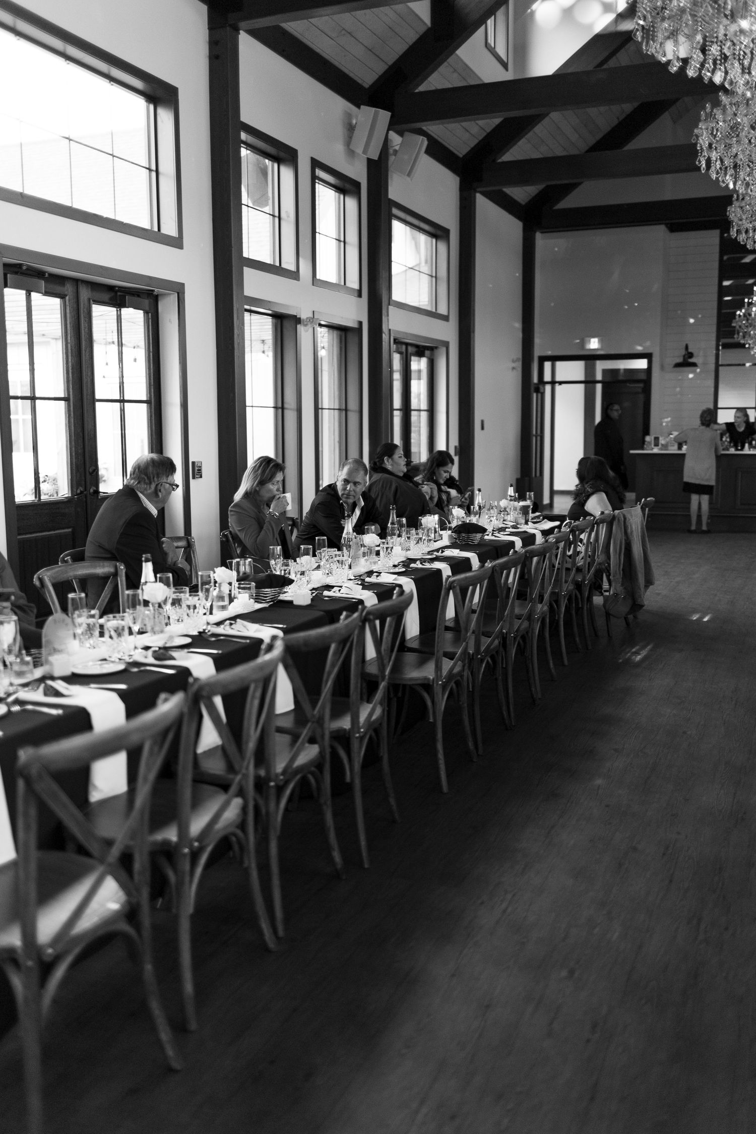 Elegant reception hall with dark hardwood floors and rows of tables set for a formal dining event at the Barn at Wind's Edge in Saskatoon.