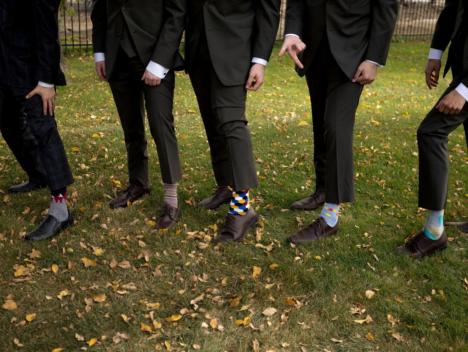Row of wedding party members' feet showing various dress shoes and socks on grass.