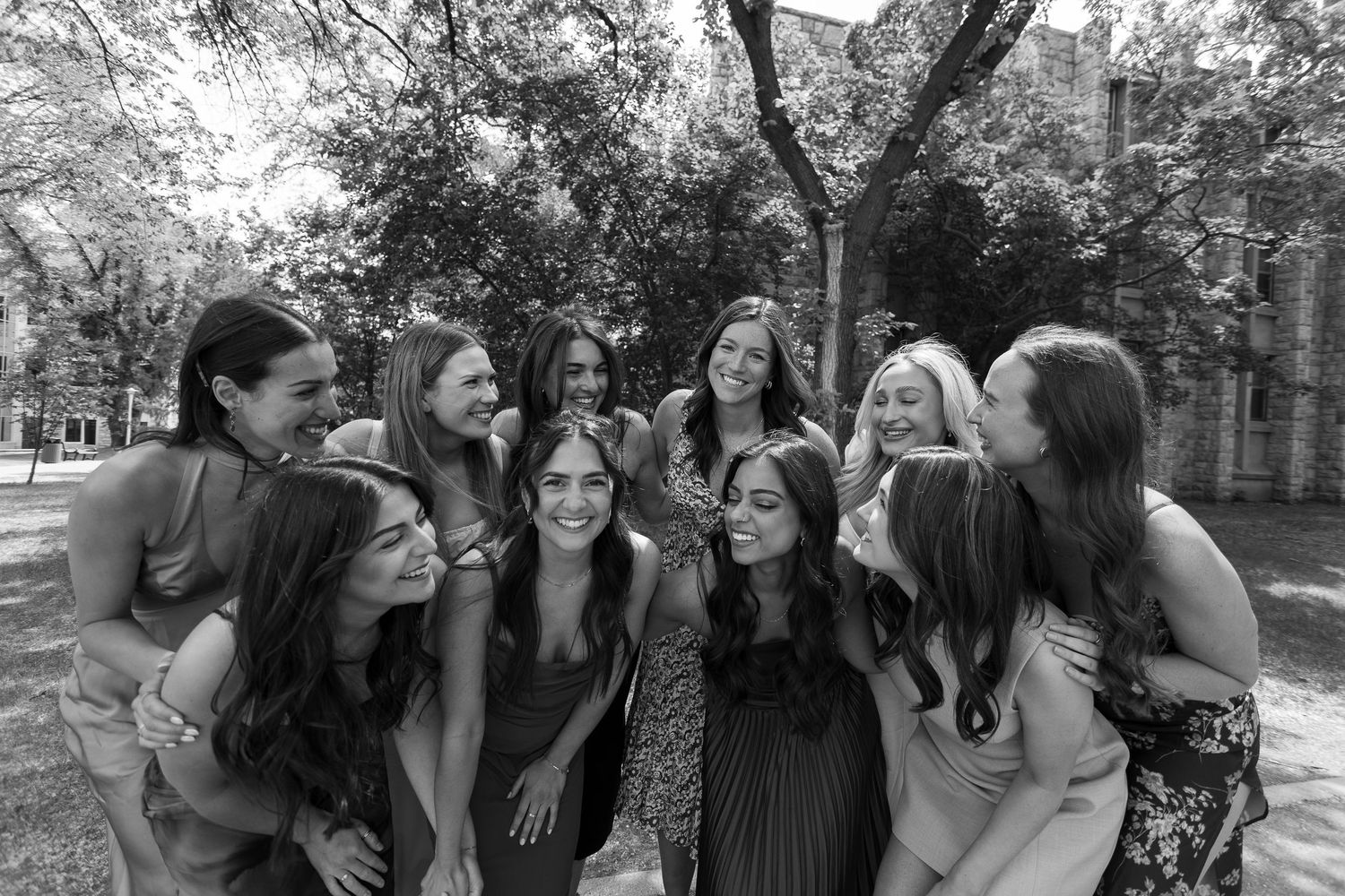Group of young women laughing and embracing outdoors on a college campus in a black and white photo.