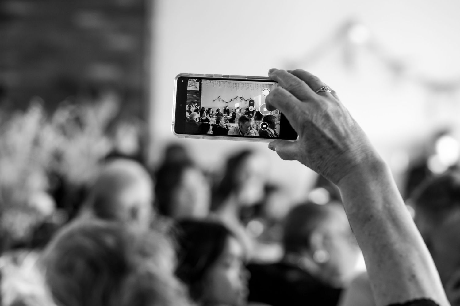 Crowd holding up phones to capture moments at wedding celebration.