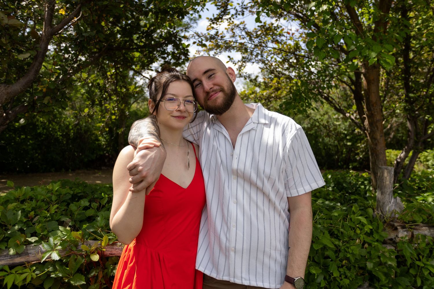 Romantic couple in a red dress and striped shirt embrace outdoors in a lush garden setting at the Berry Barn in Saskatoon, Sask.