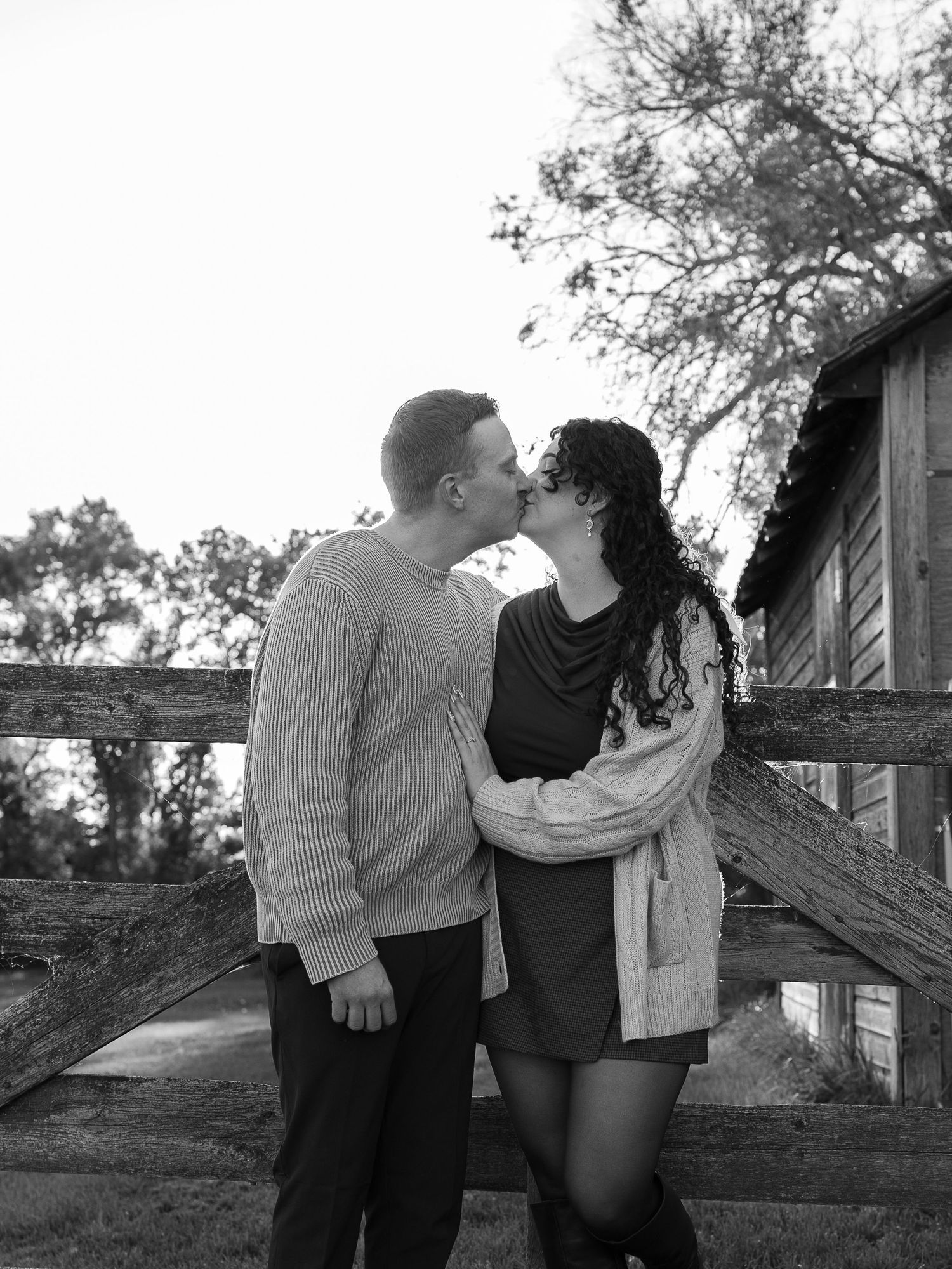 A couple shares a tender moment against a wooden fence in black and white photography.