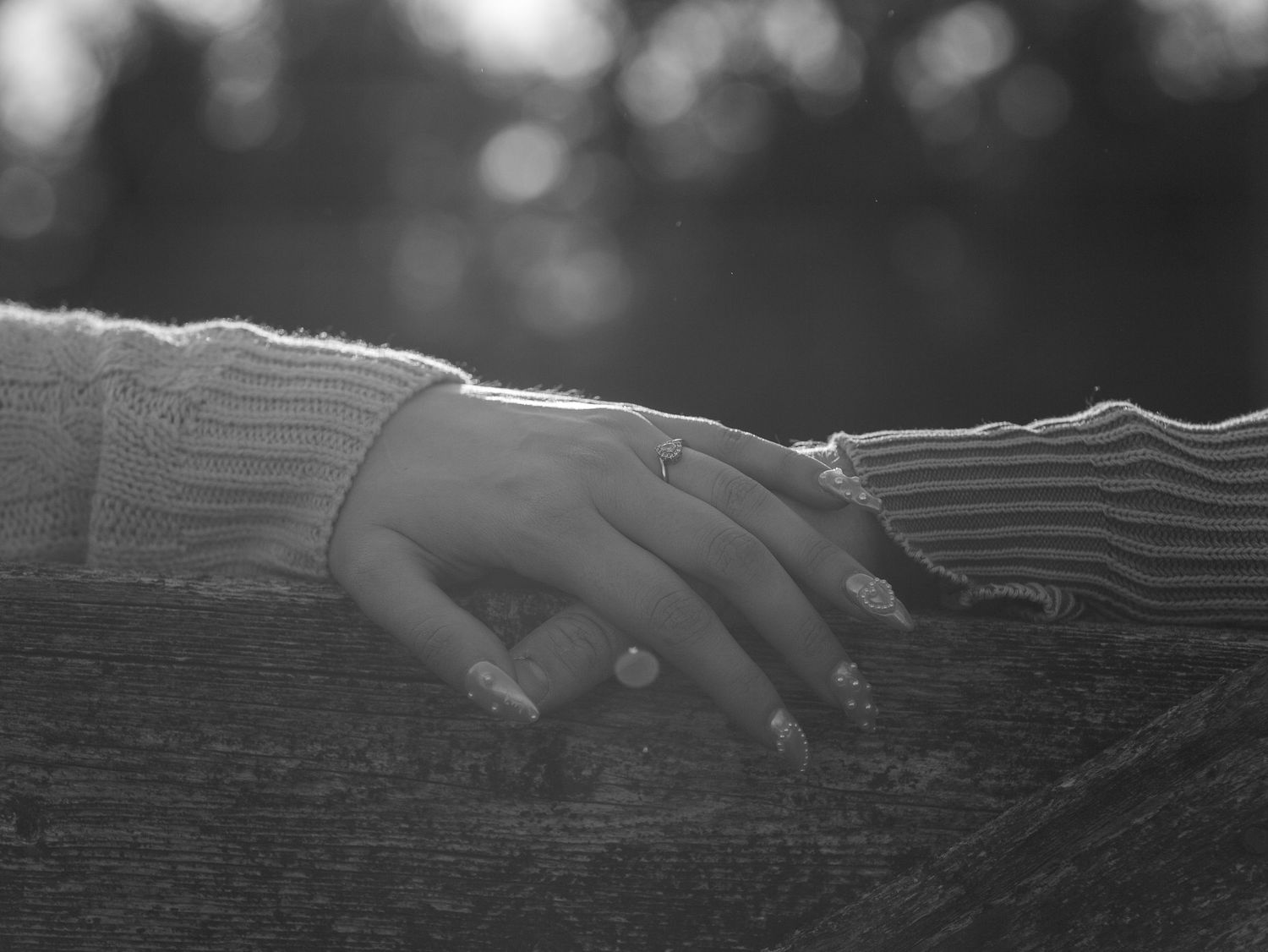 Two hands with engagement rings touch in black and white lighting.