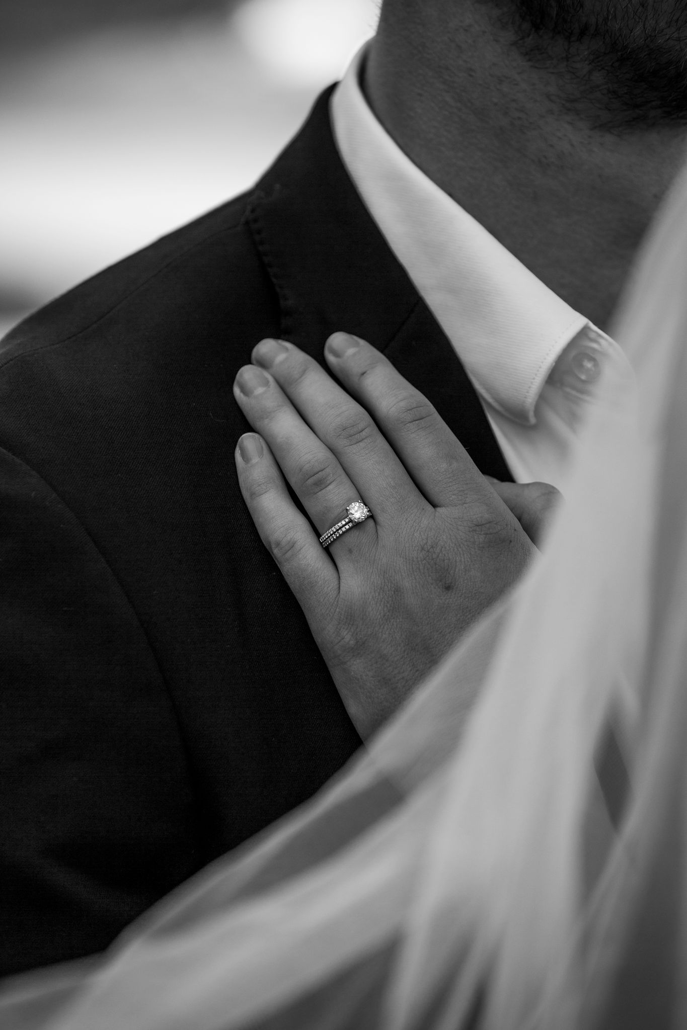 Close-up black and white detail of hands wearing formal attire and wedding rings.