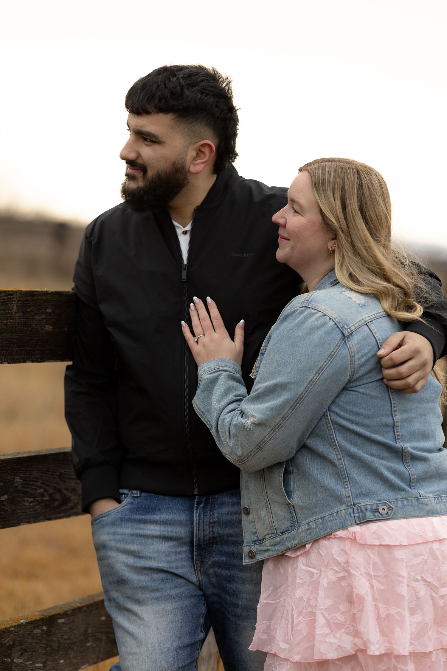 Couple shares tender moment against wooden fence at sunset.