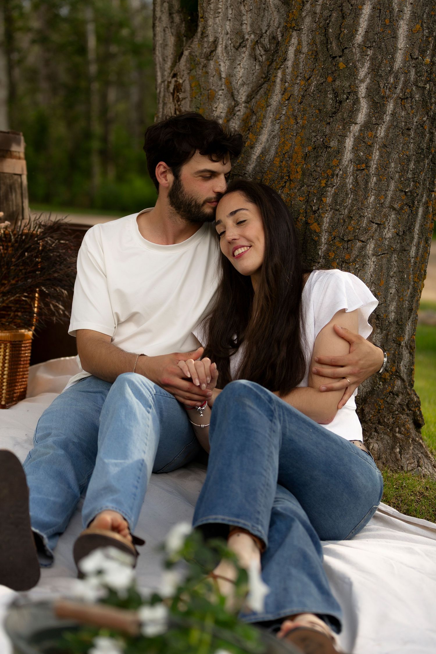 Casual couple sharing intimate moment while sitting on blanket beneath tree.