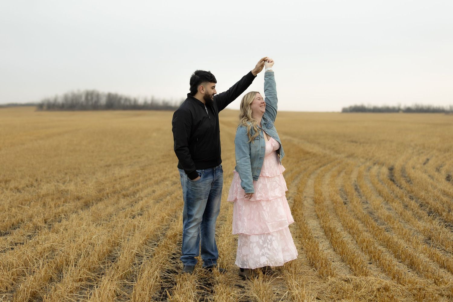 A couple walks hand in hand through a vast golden wheat field at sunset.