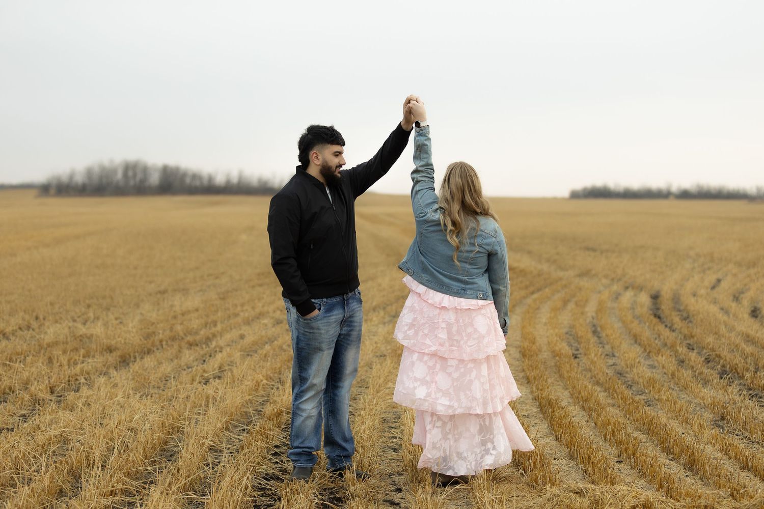Couple holding hands raised in celebration while standing in a harvested wheat field.