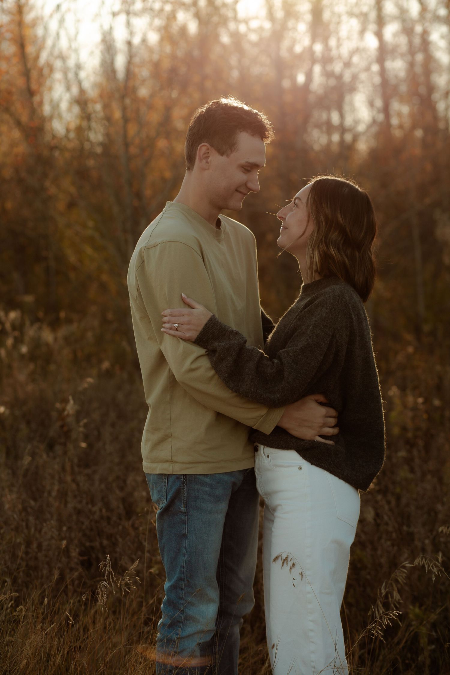 Couple embracing and smiling at each other in a golden autumn field at sunset.