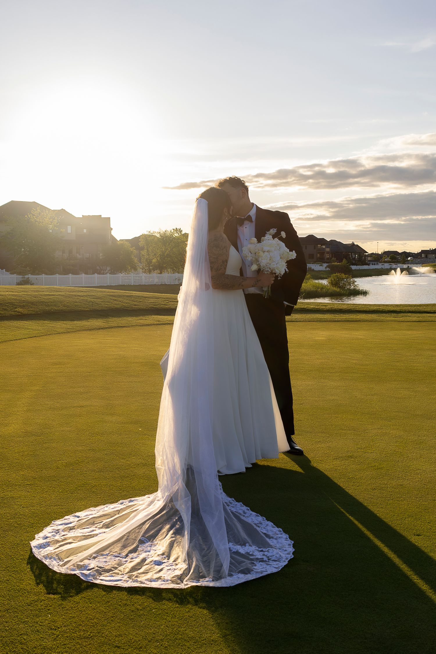 A bride's flowing white dress train spreads elegantly across a green golf course at sunset.