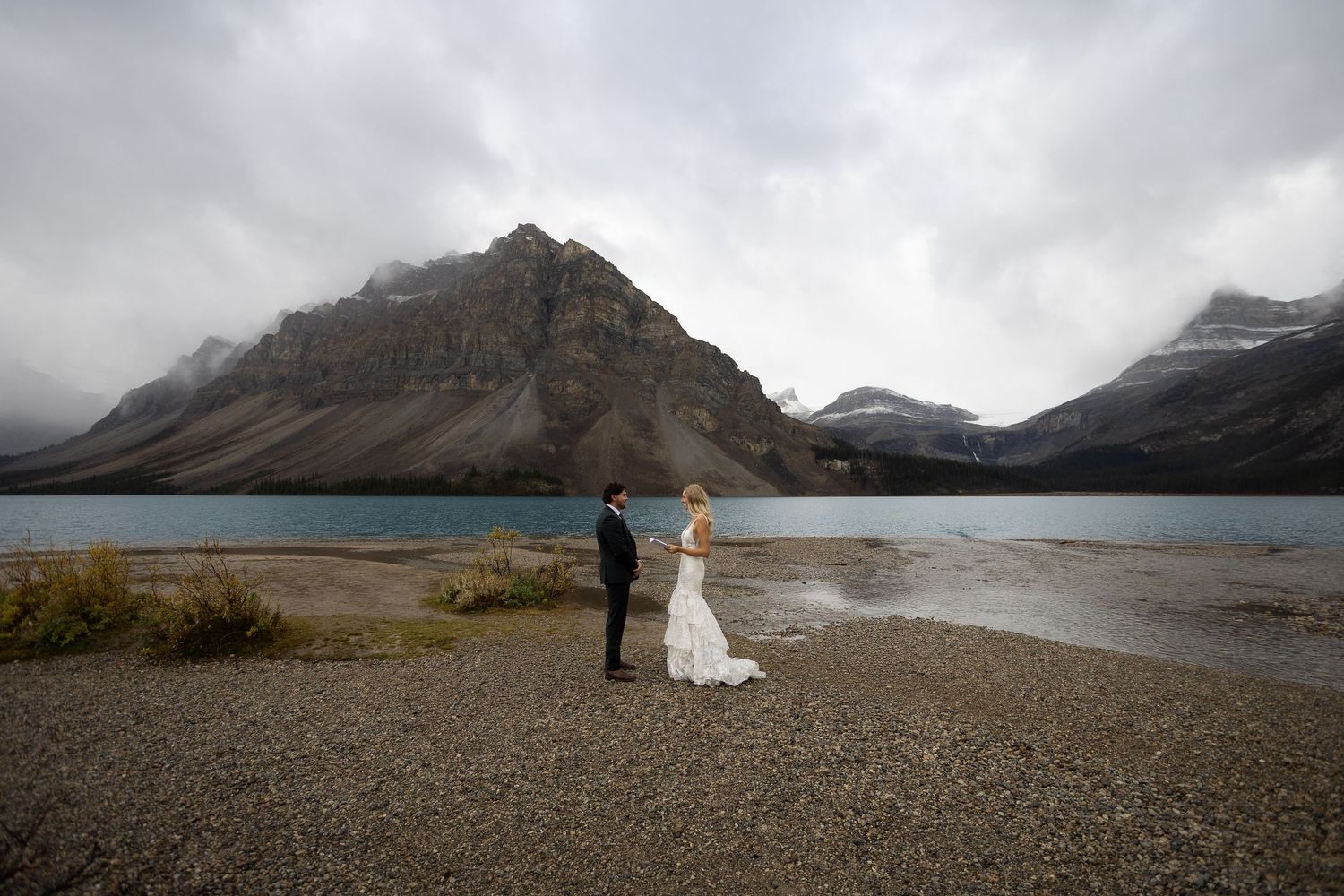 Bride and groom exchange vows by a glacial lake with dramatic mountain backdrop in the Canadian Rockies.
