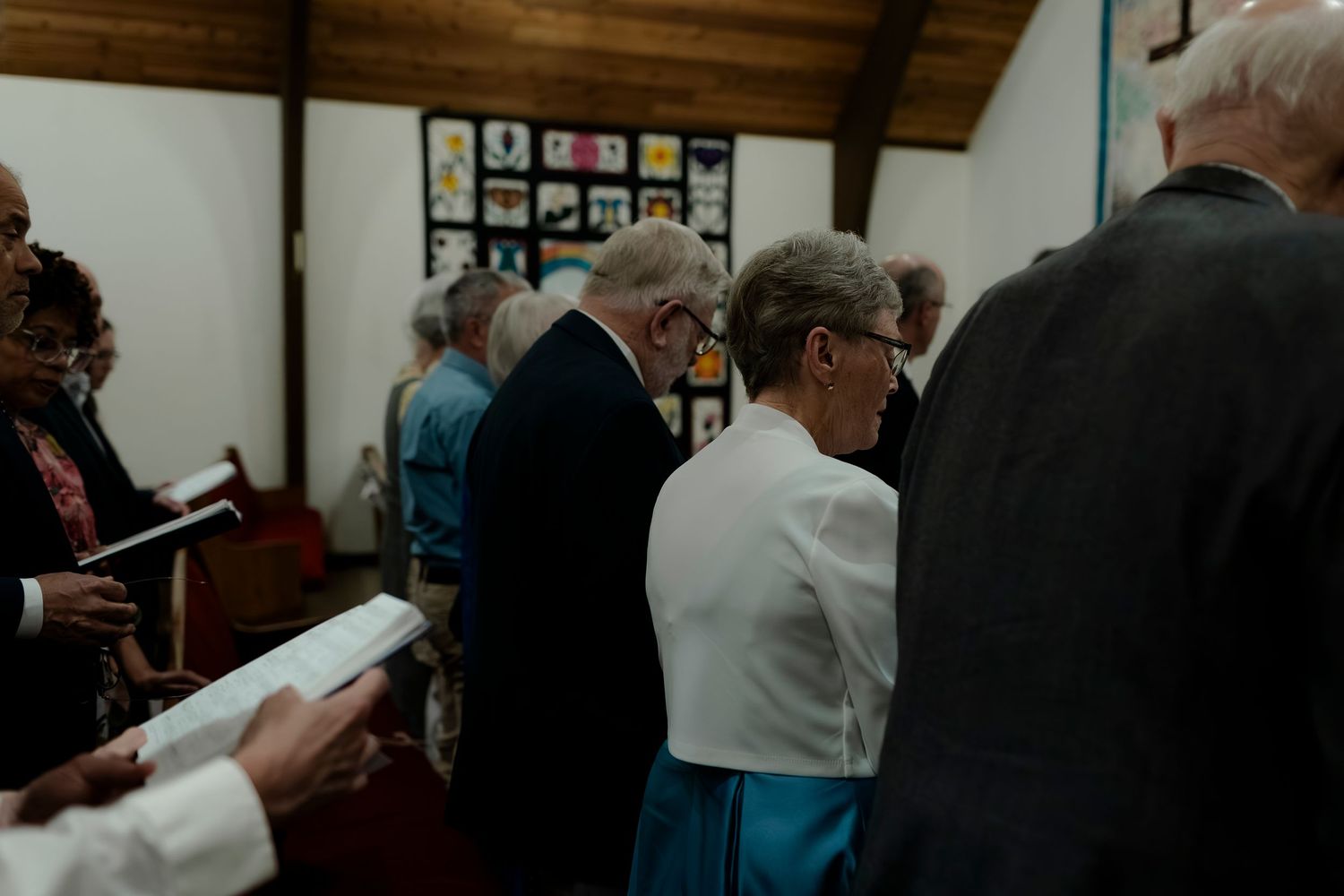Wedding guests seated in wooden pews during an indoor church ceremony.