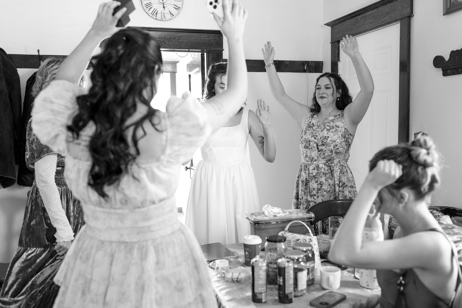Black and white photo of bridesmaids celebrating with raised hands during wedding preparations indoors.