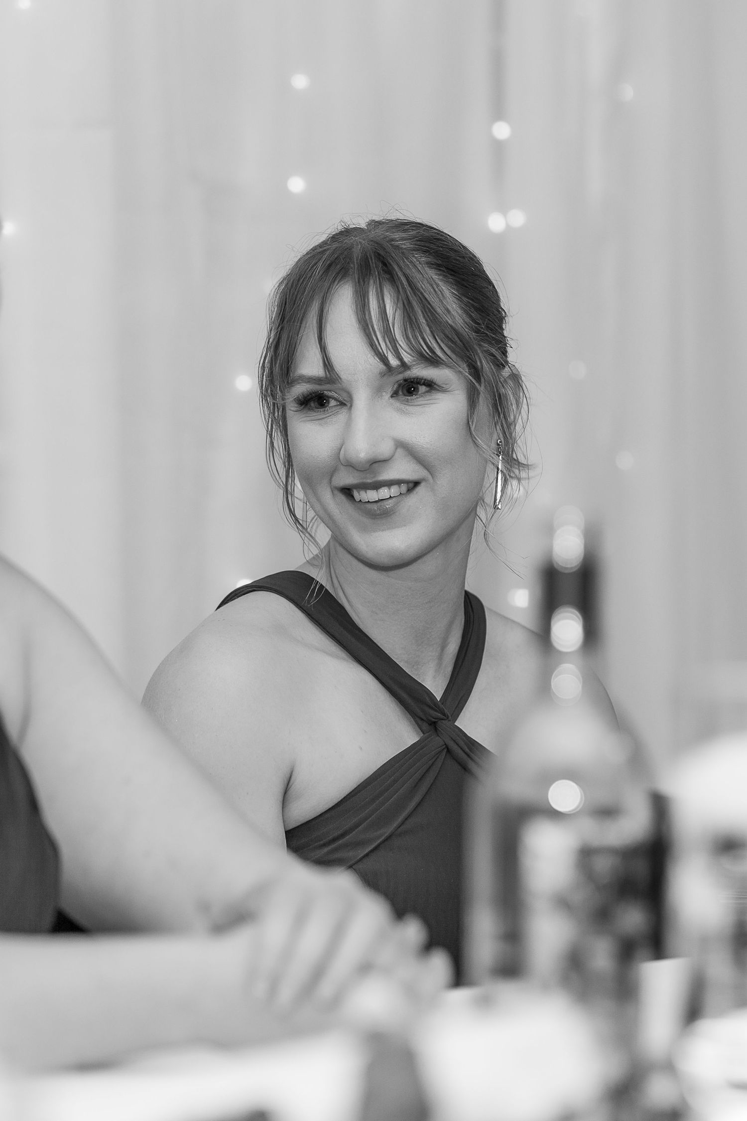 A smiling woman in an elegant dress sits at a table at a formal event, captured in black and white photography.