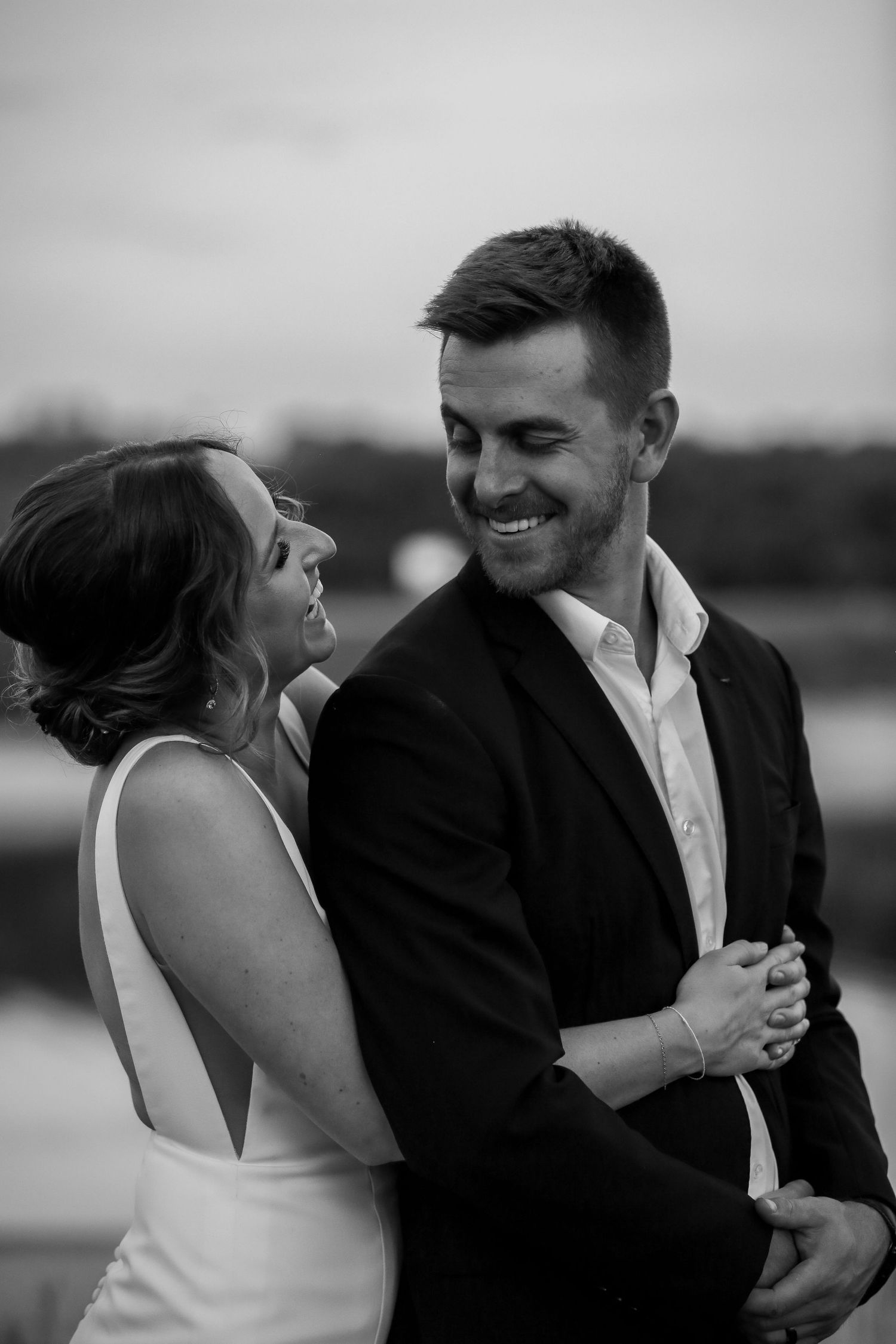 Black and white candid wedding photo showing a joyful couple sharing an intimate moment outdoors.
